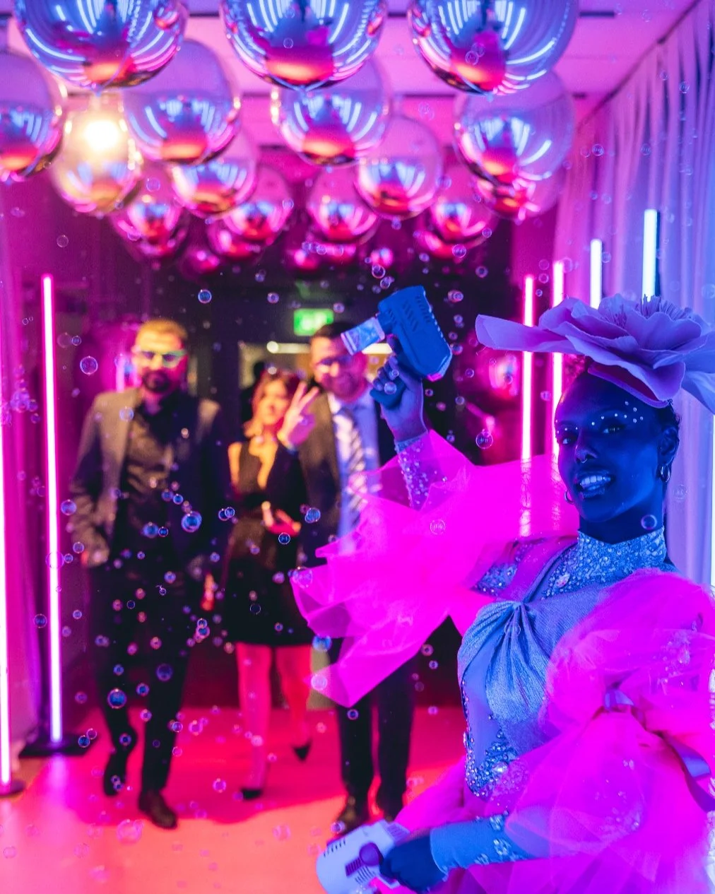A female standing with bubbles in a silver balloons environment.
