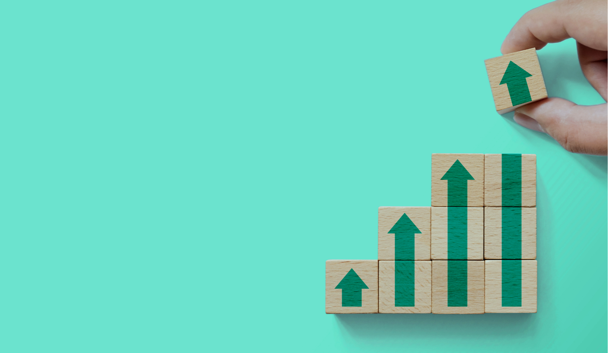 Stacked wooden blocks with green upward arrows drawn on them, arranged in increasing height from left to right, with a hand placing the top block.