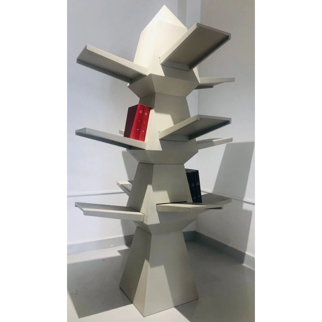 Étagère moderne en forme de sculpture géométrique avec quelques livres colorés posés dessus, située dans un espace intérieur.