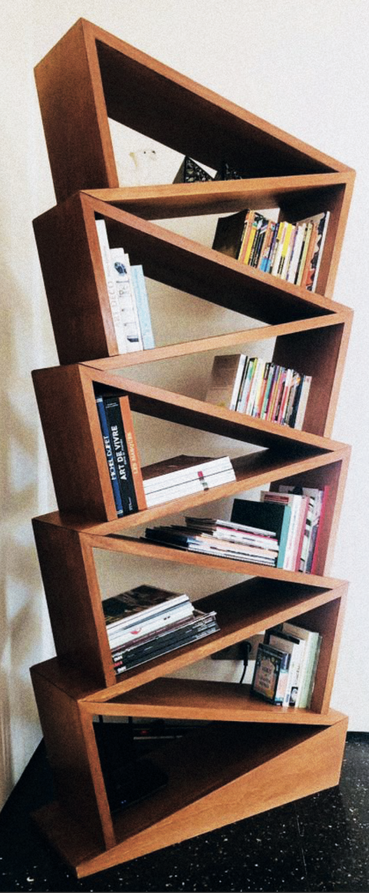 Bibliothèque en bois inclinée remplie de livres.