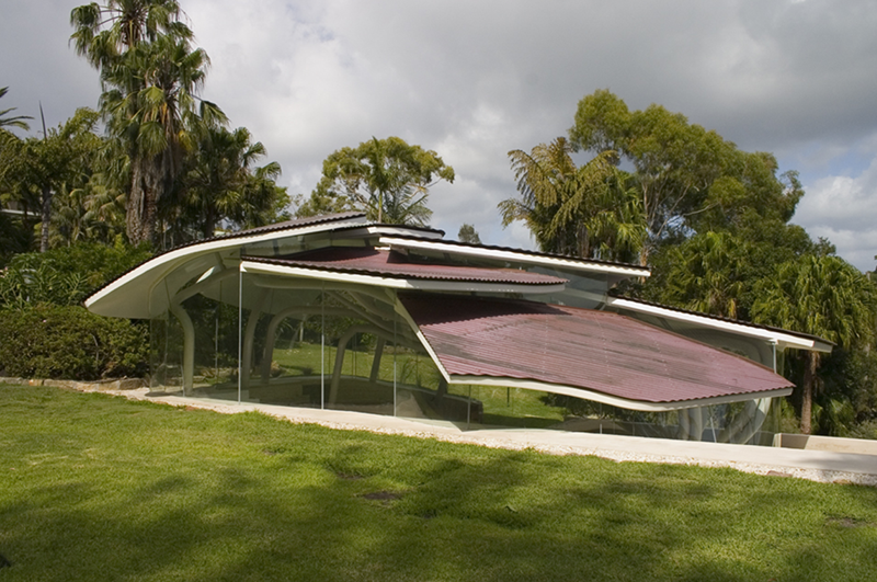 Maison moderne avec toit incurvé, entourée de végétation et d'arbres tropicaux.