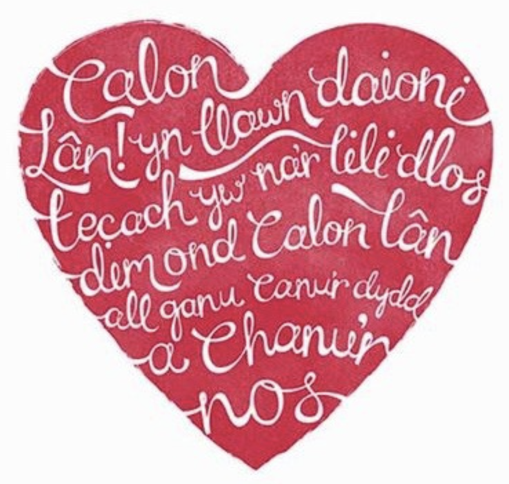 Red heart with white handwritten Welsh text inside.