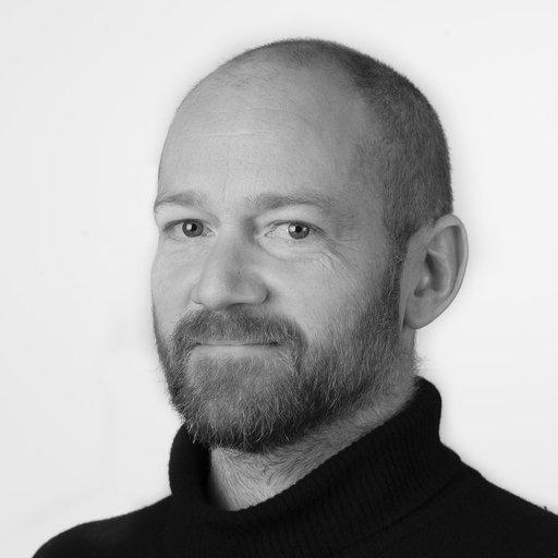 Black and white portrait of a man with a beard and short hair, wearing a black turtleneck.