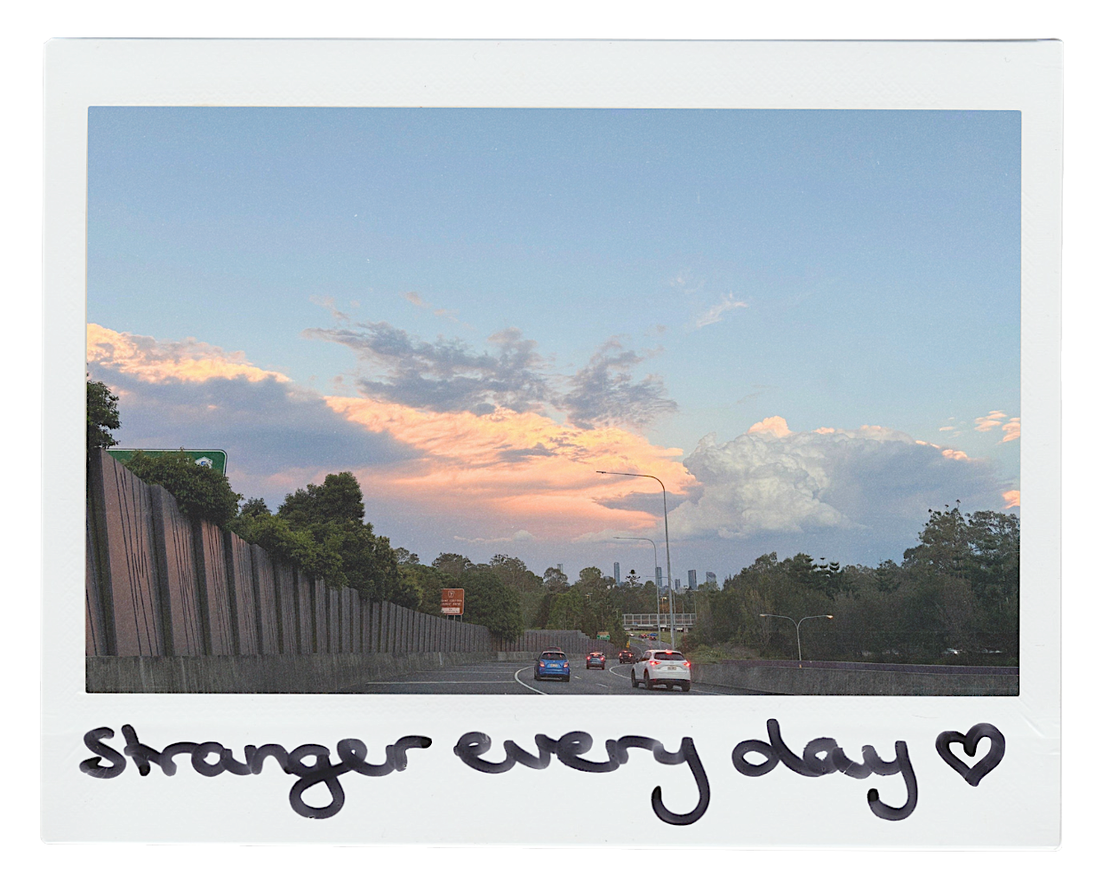 A polaroid of a sunset over a motorway. On the bottom of the frame, 'Stranger Every Day' is written in black marker.