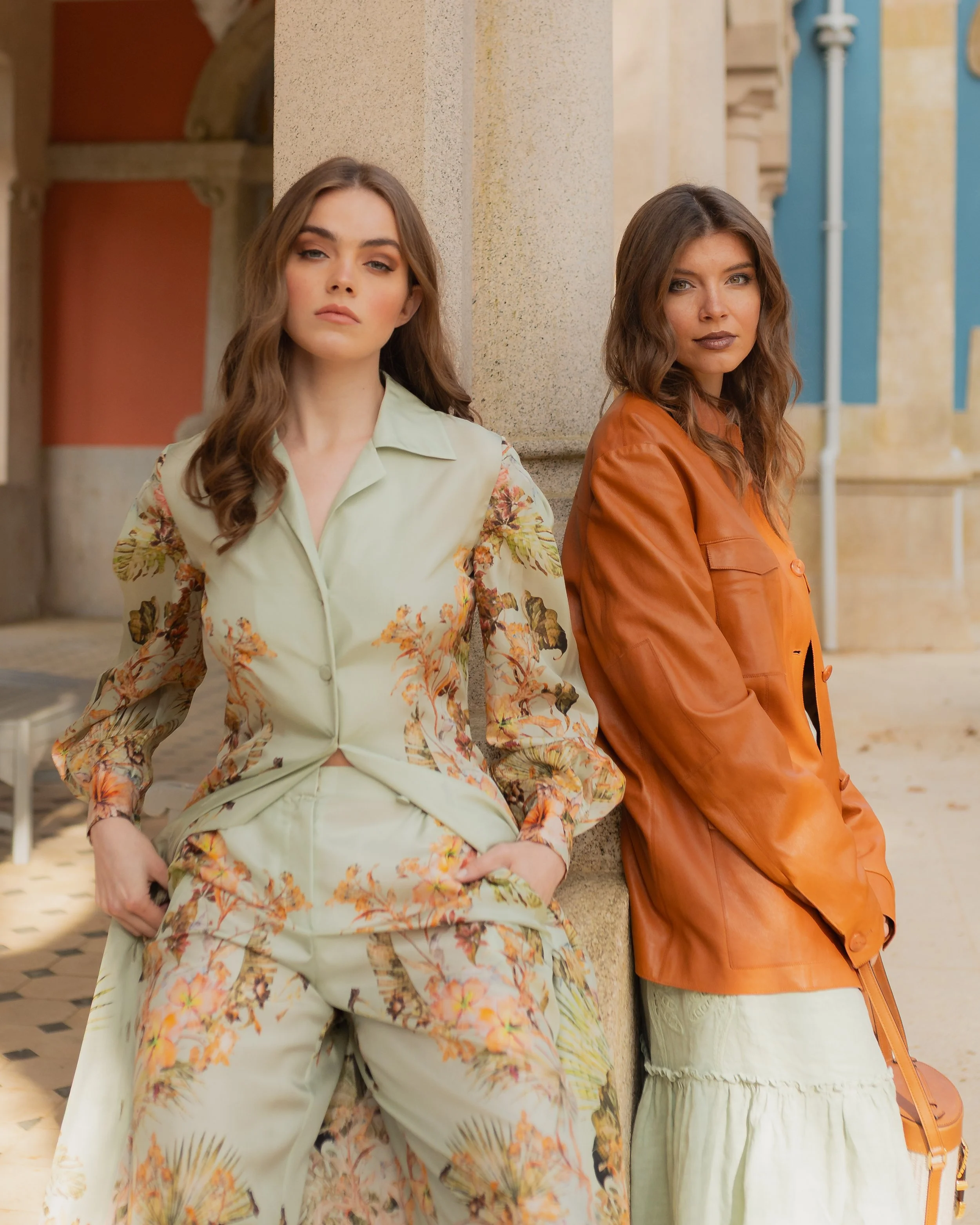 Two women standing outdoors; one in a floral outfit, the other in a brown jacket.