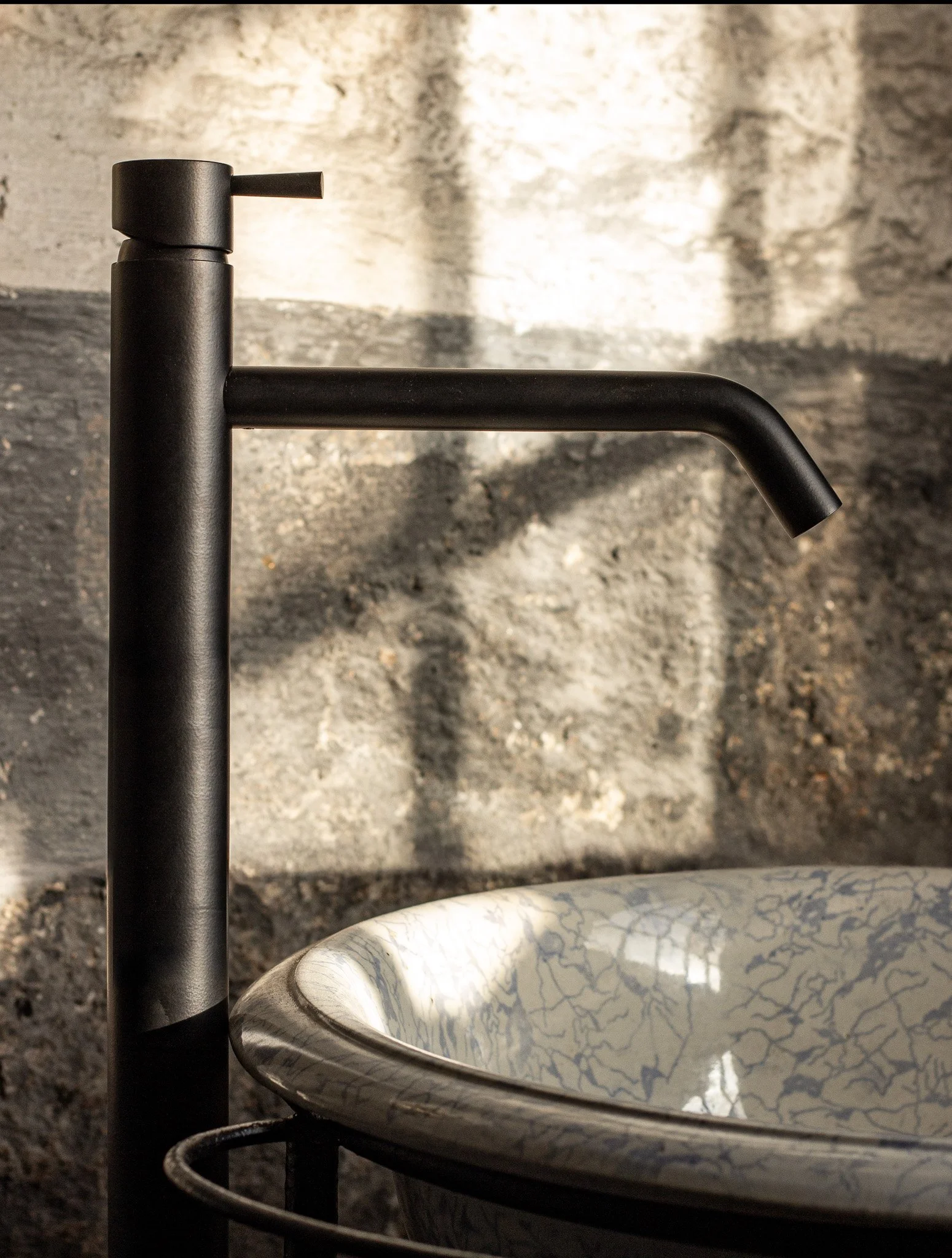 Imagem de uma bancada de cozinha preta com torneira e uma pia de mármore branco com detalhes em azul. No fundo, parede de pedra com textura rústica.