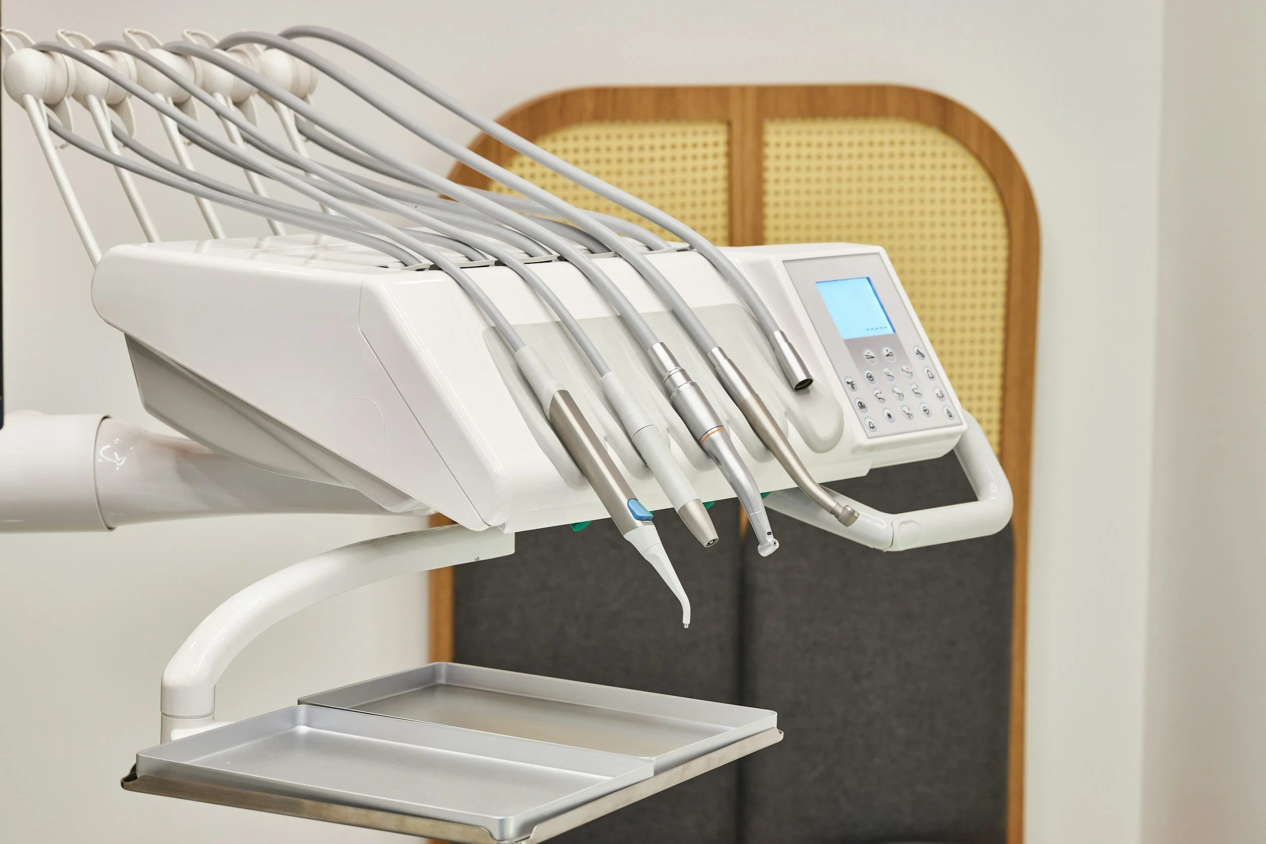 A dental dental unit with various handheld dental instruments on a white cart in a clinical setting.