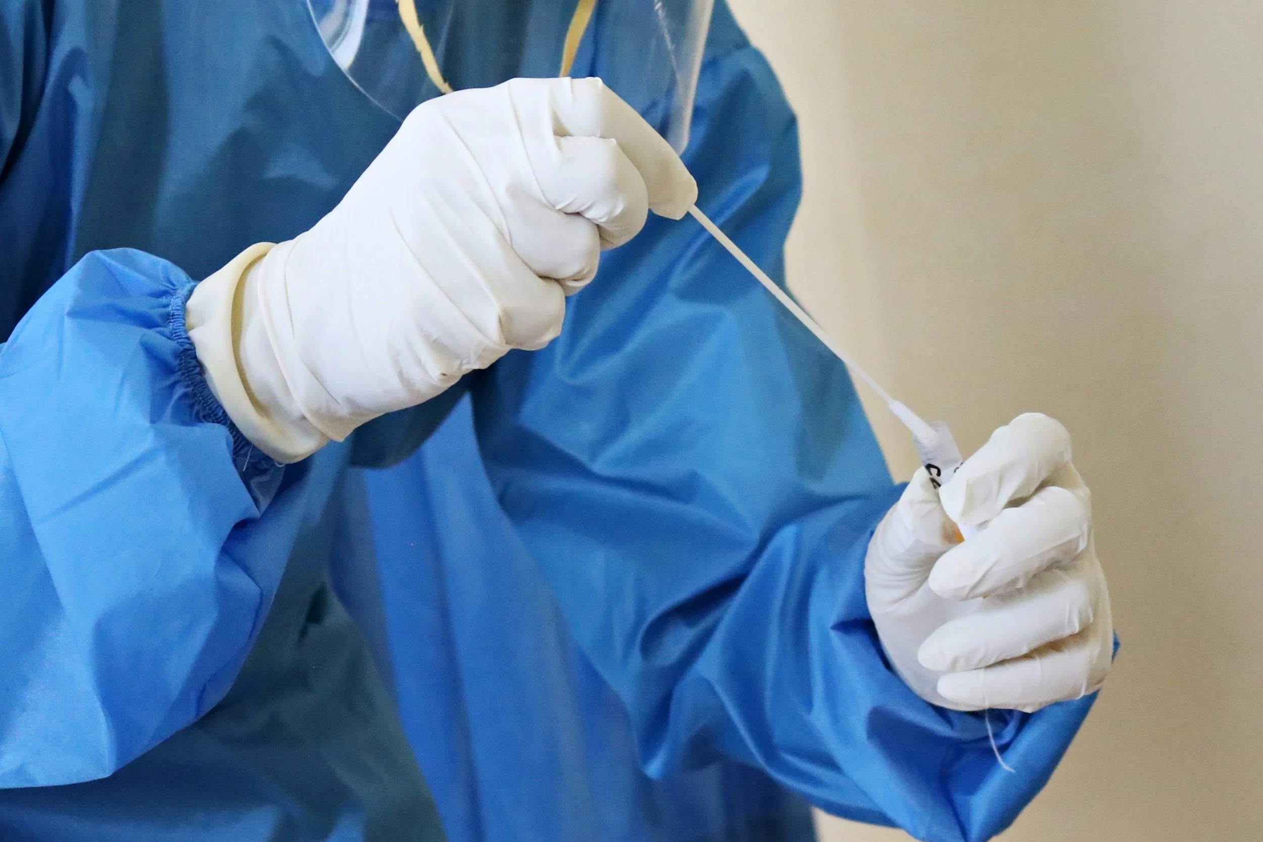 A healthcare professional wearing a blue gown and white gloves preparing swabbing a sample into a tube.