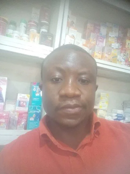 A man in a pharmacy, with shelves of medicines and health products in the background.
