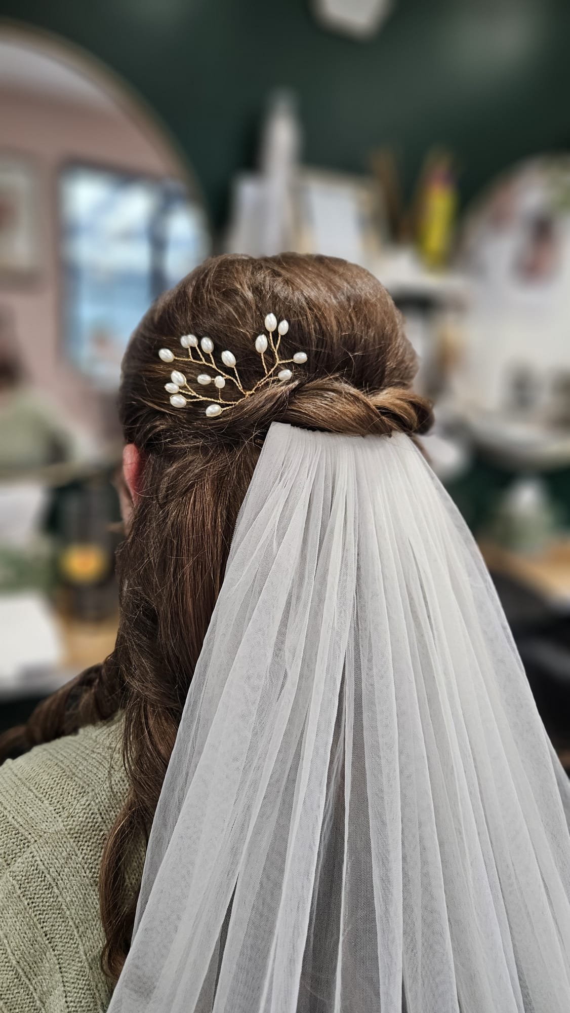 Back of a bride's head with a veil and a pearl hair accessory, styled in an elegant updo.