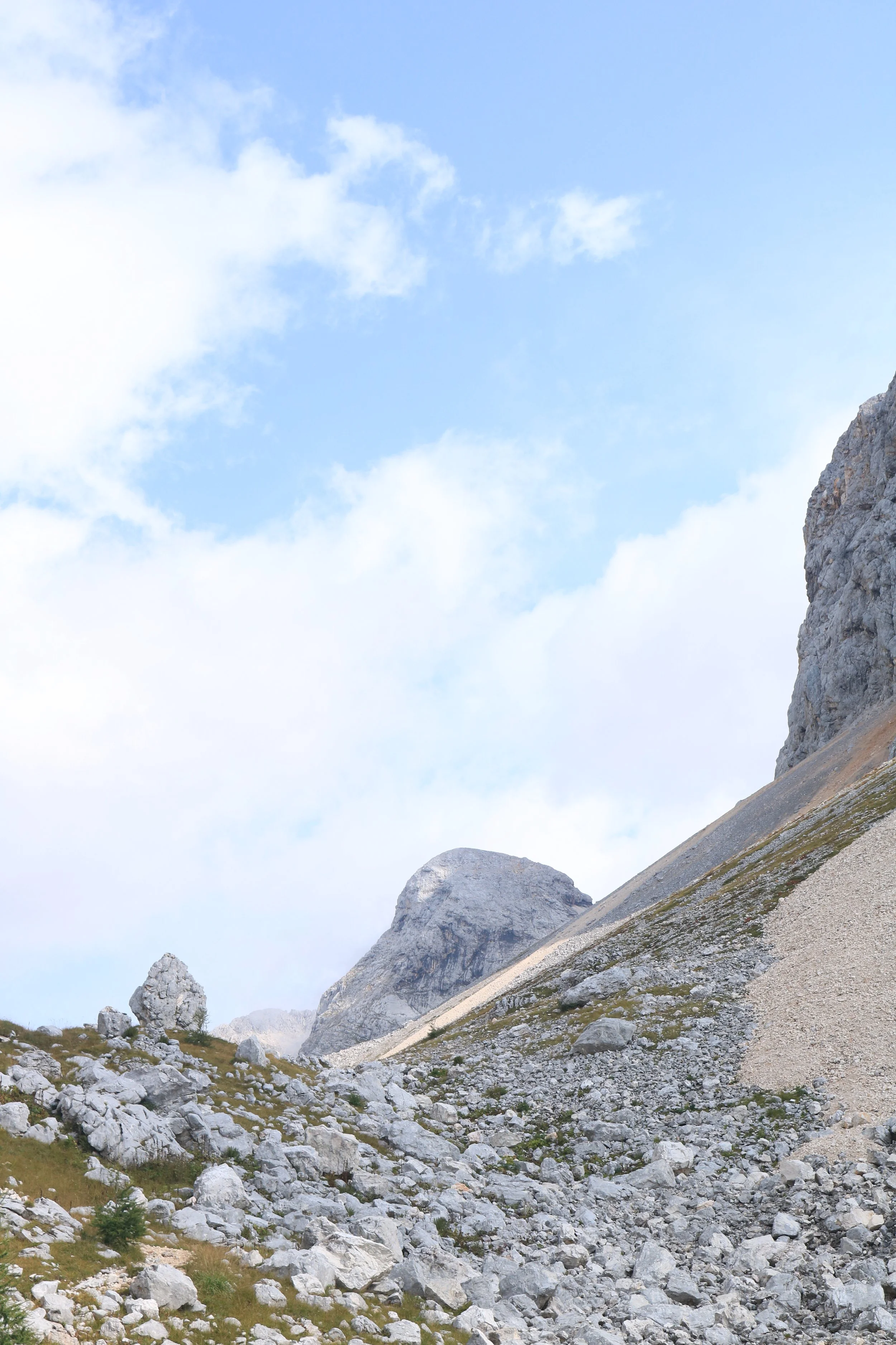 Mountain landscape with rocky terrain, large rock formations, and a partly cloudy blue sky.