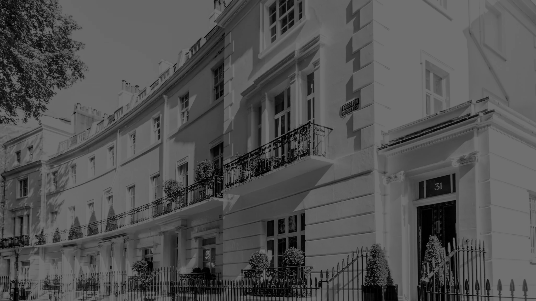 Black and white photo of a large, elegant multi-story residential building with balconies, decorative molding, and a gated entrance, located on a street corner.