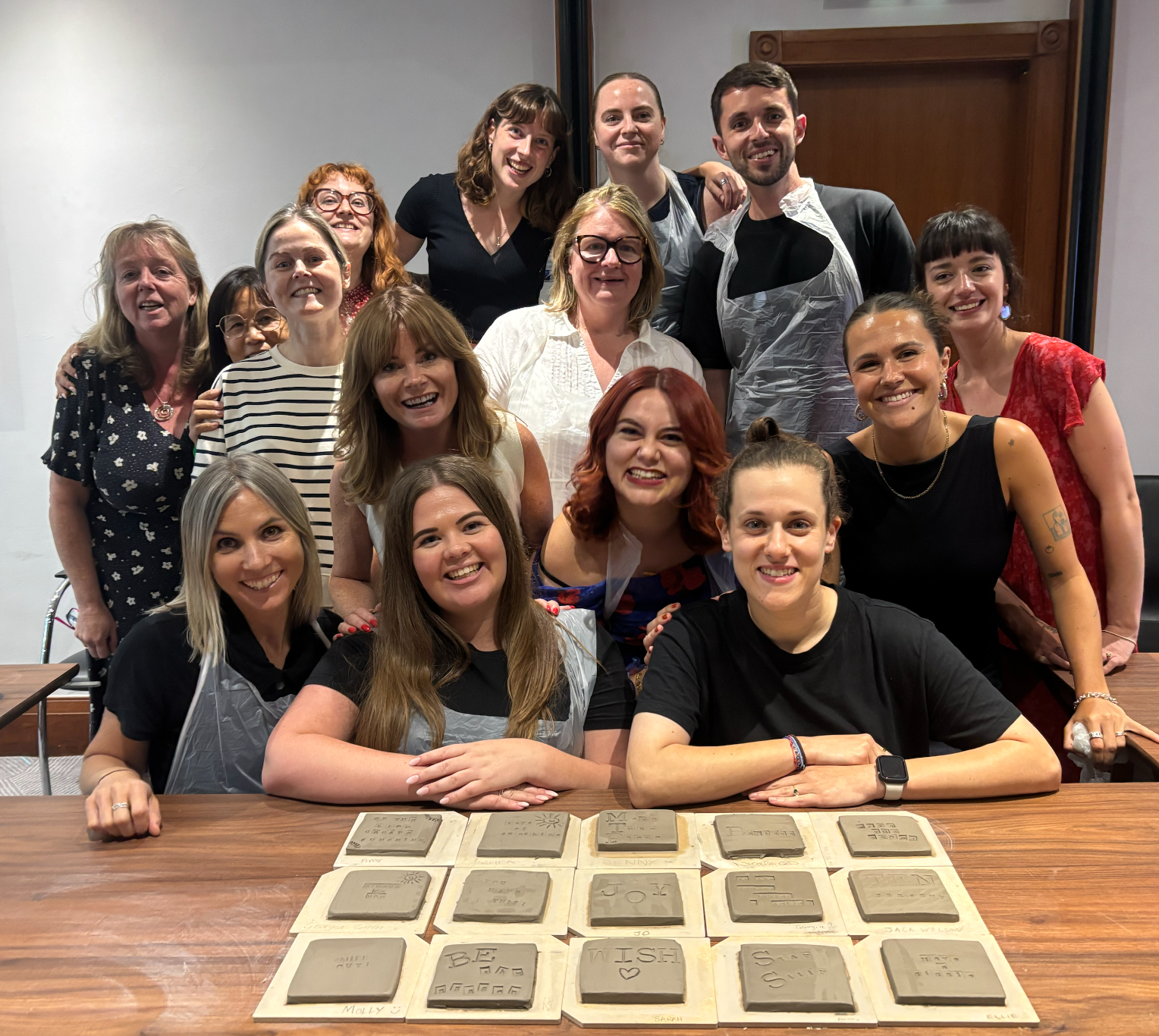 A group of smiling people group proudly in front of a series of clay coasters each bearing personal and company values.