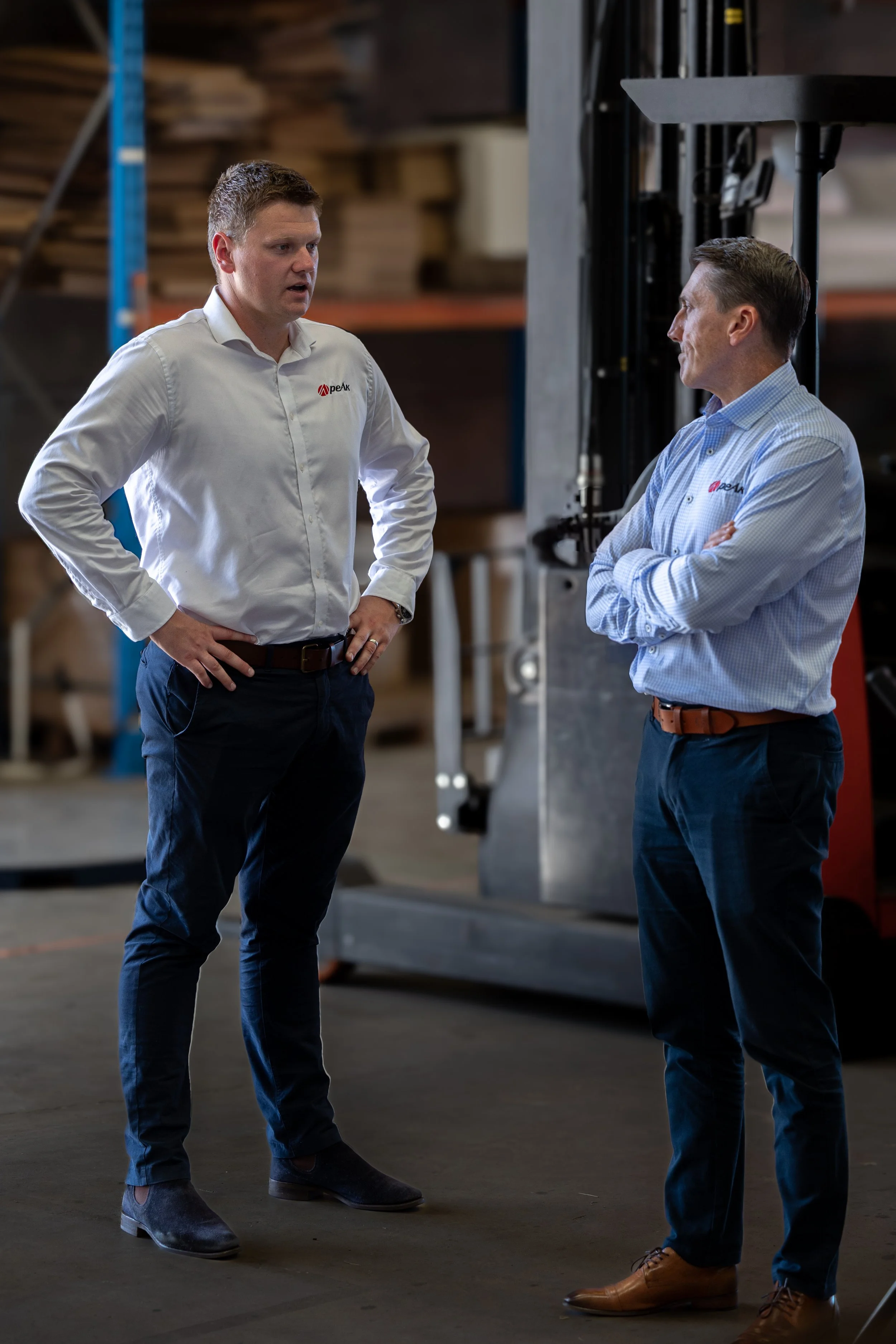 Two men in business casual attire standing and talking in a warehouse environment.