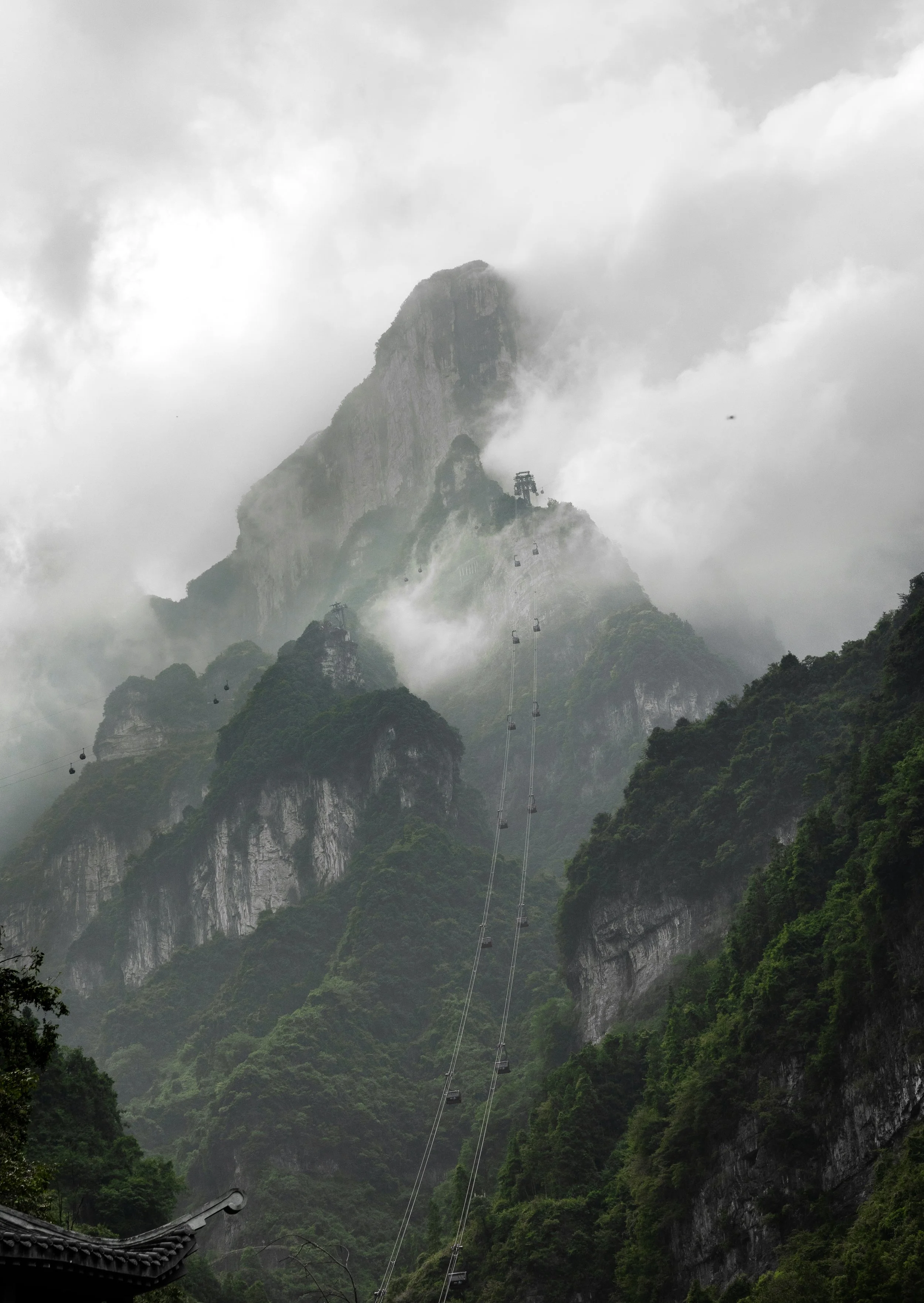 Mountain landscape with cable cars ascending through clouds and lush greenery.