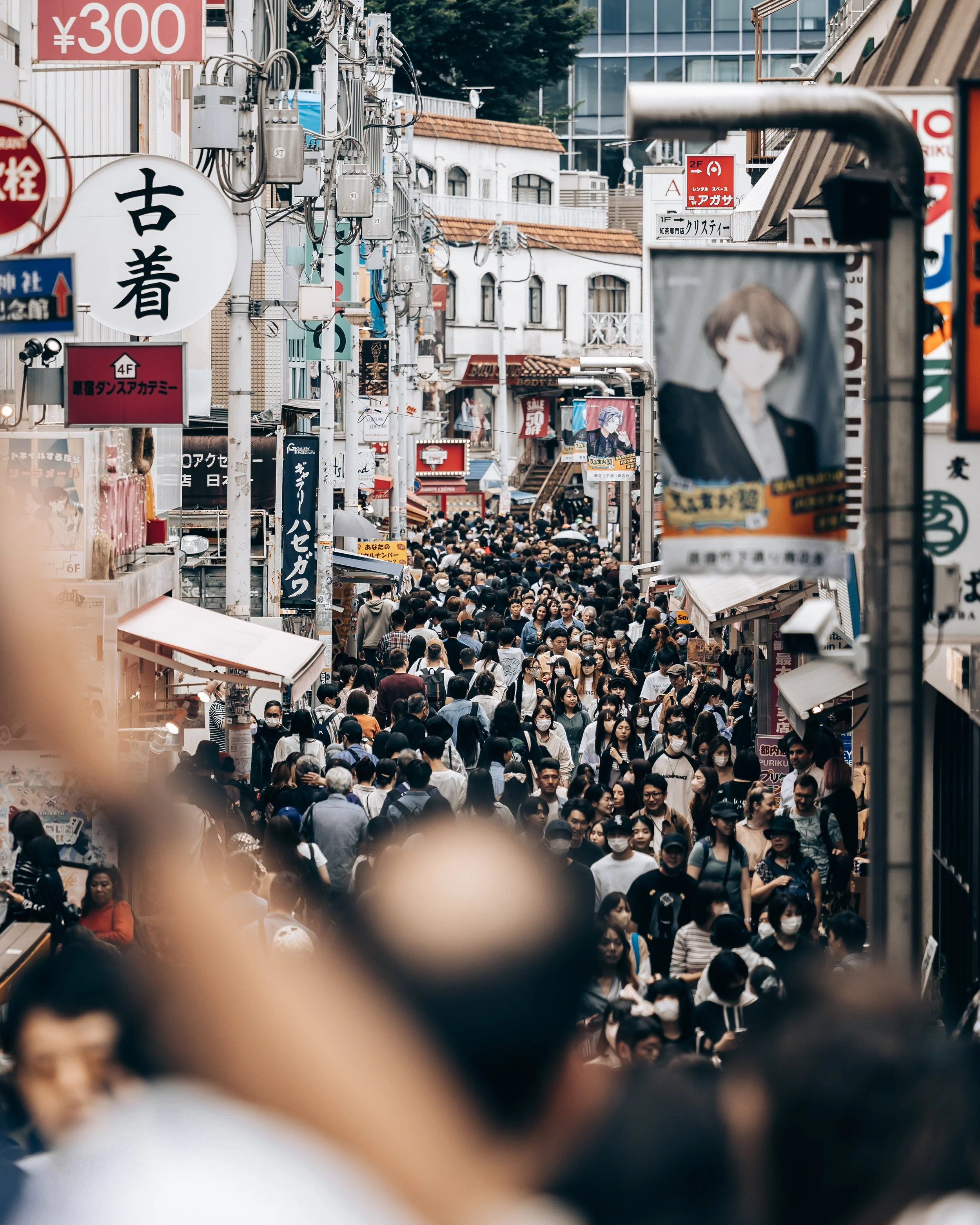 Crowded urban street in Japan with many pedestrians, shops, and signs in Japanese.