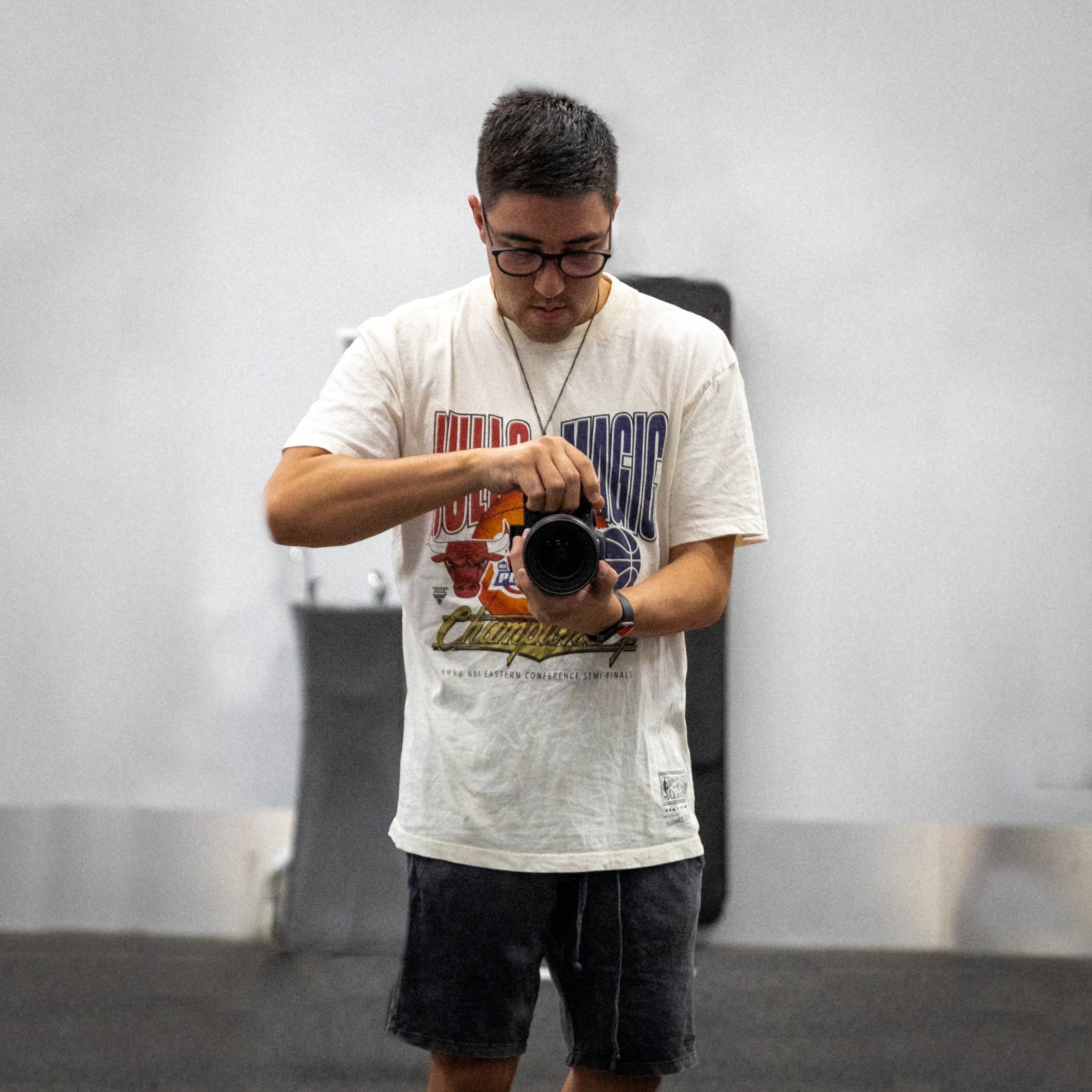 Person adjusting lens on a camera indoors, wearing glasses and a graphic t-shirt.