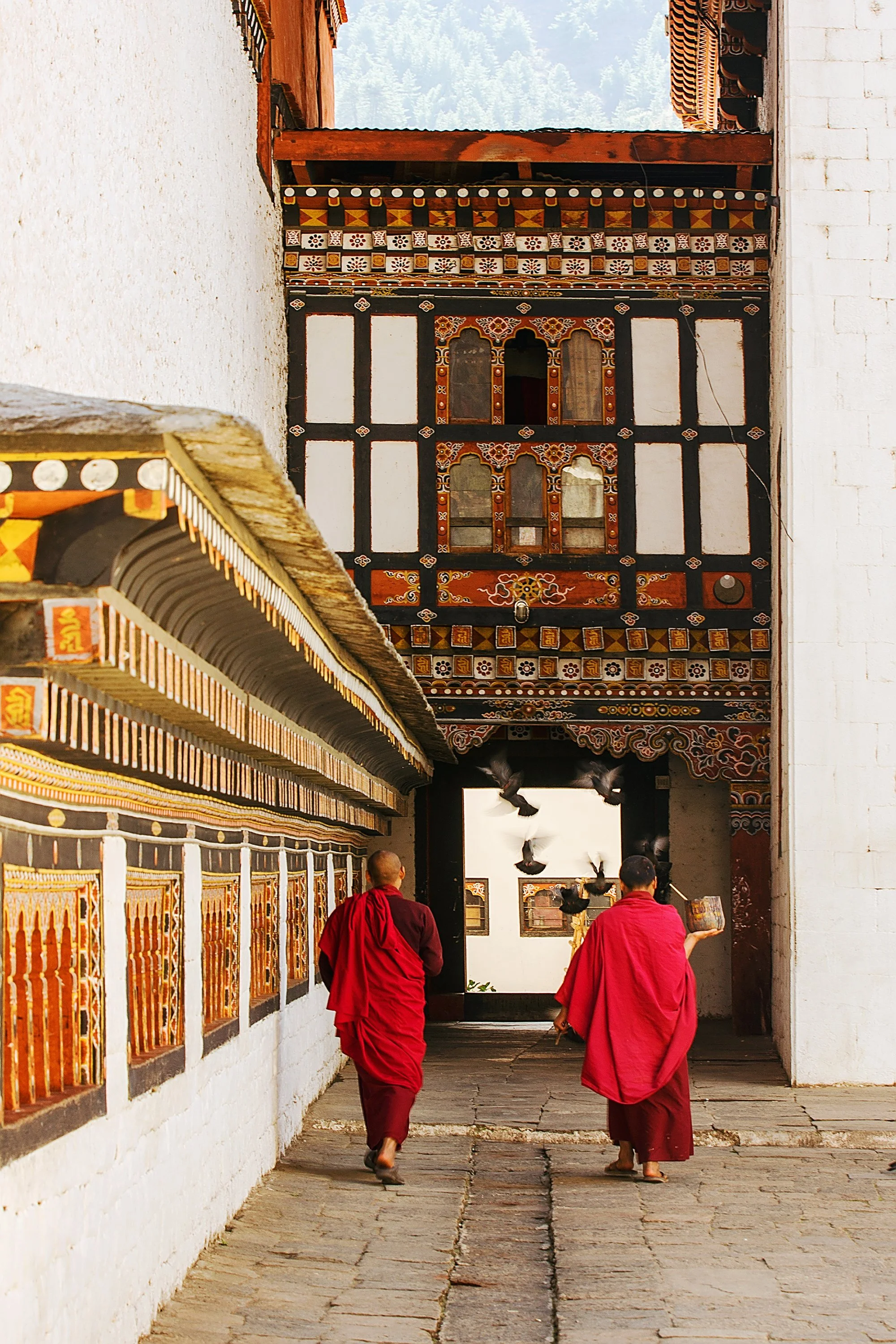 Zwei Mönche in roten Roben gehen durch einen kunstvoll verzierten Bogen in einer traditionellen tibetischen Tempelanlage.