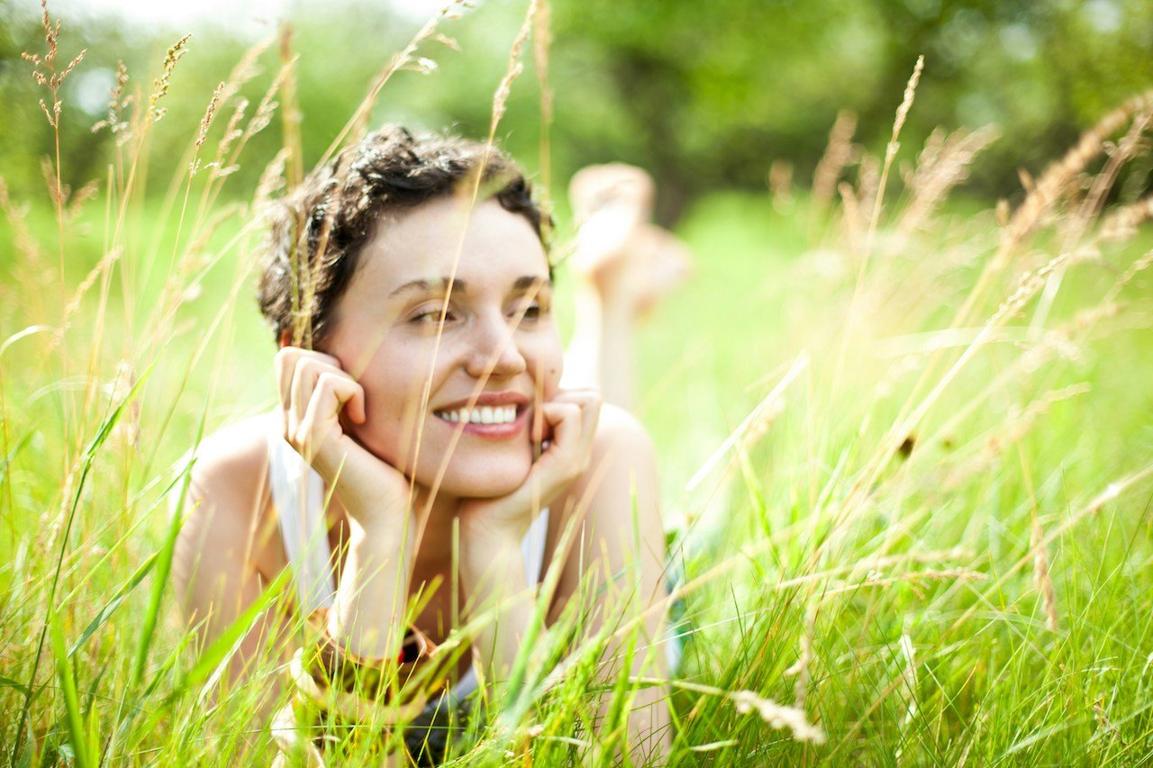 woman with can on hands lying in grass