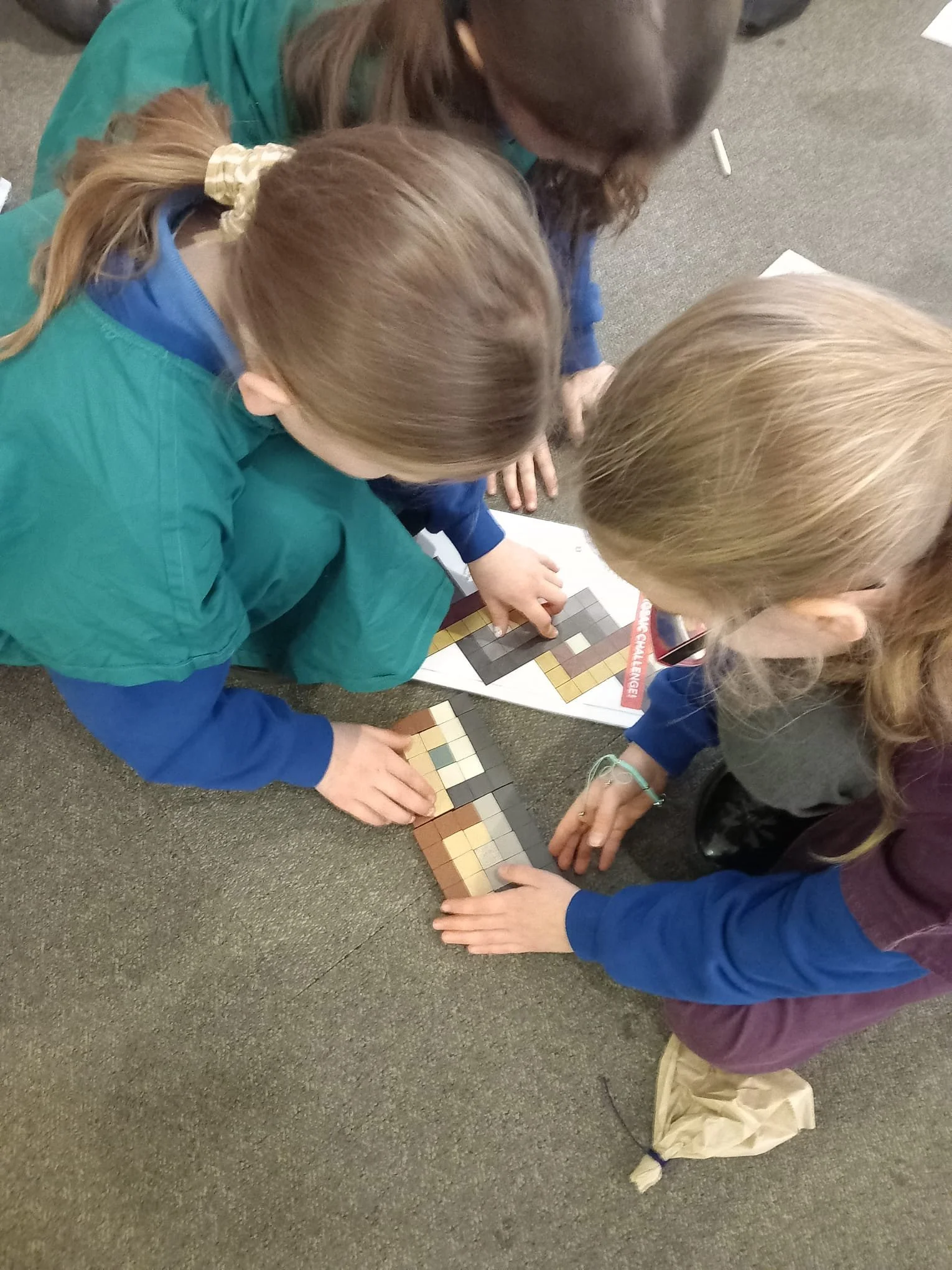 Three children are gathered around and working together on a puzzle made of small Roman colored square tiles on the floor.