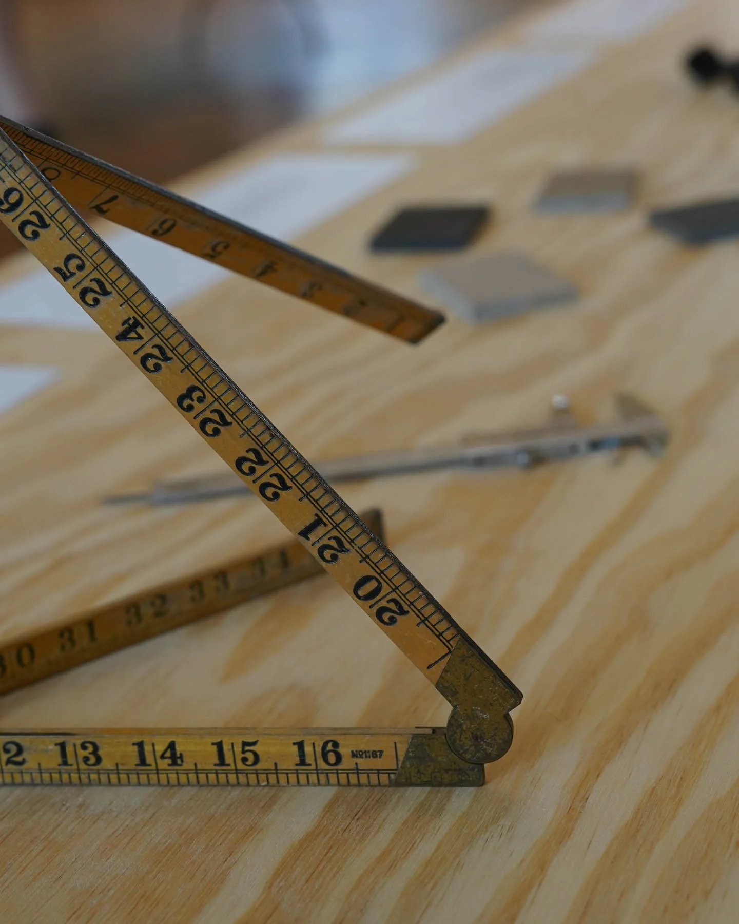 Close-up of a wooden folding ruler with measurements in inches, partially extended, on a wooden surface with several black and gray tiles or samples in the background.
