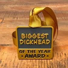 Novelty award plaque with humorous text, gold color, wooden background.