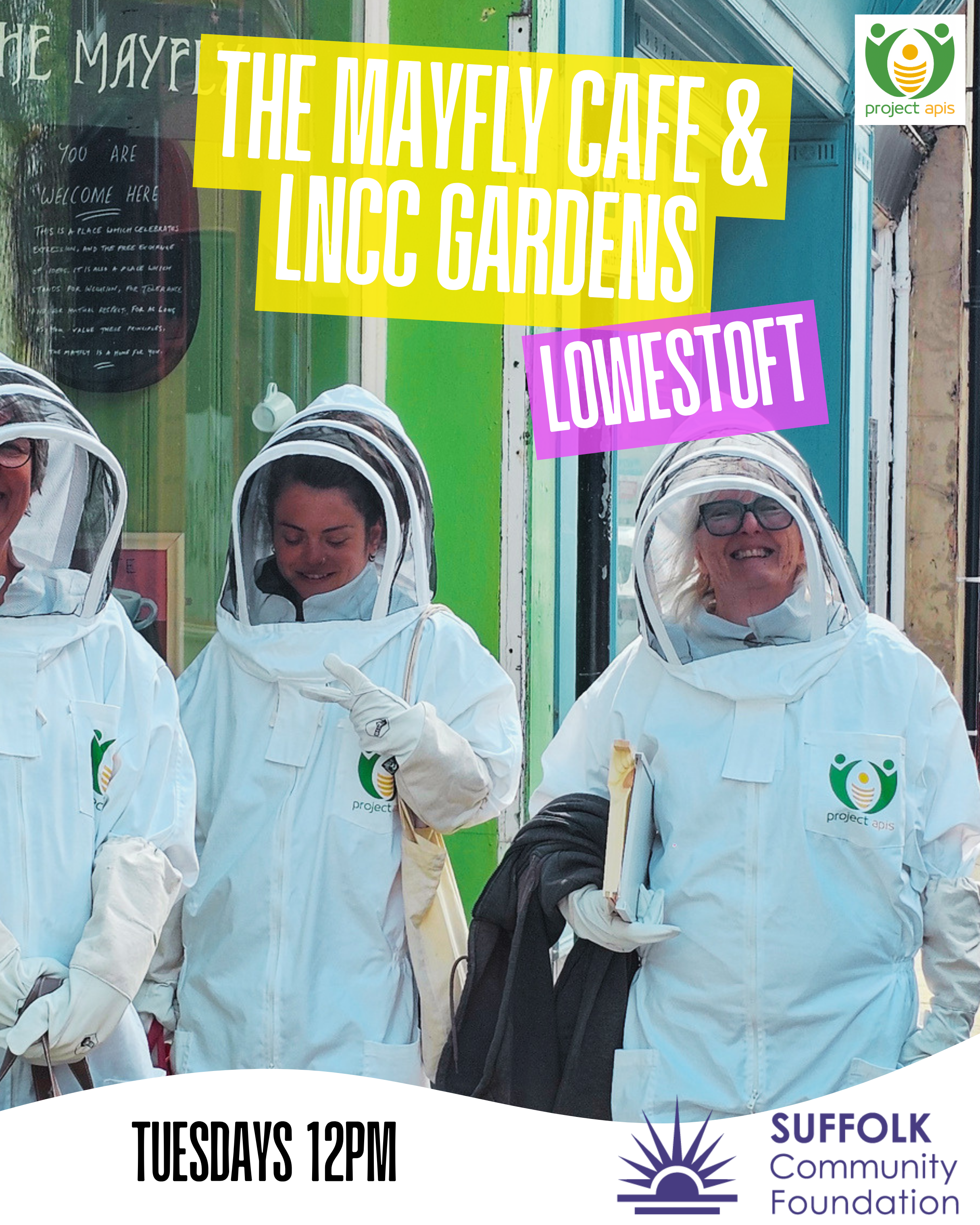 People dressed in white protective suits with mesh face coverings, standing outdoors in front of a colorful storefront with signs and logos, including the Project Apis logo and the Suffolk Community Foundation logo, promoting a community event at The Mayfly Cafe and Incu Gardens on Tuesdays at 12 PM.