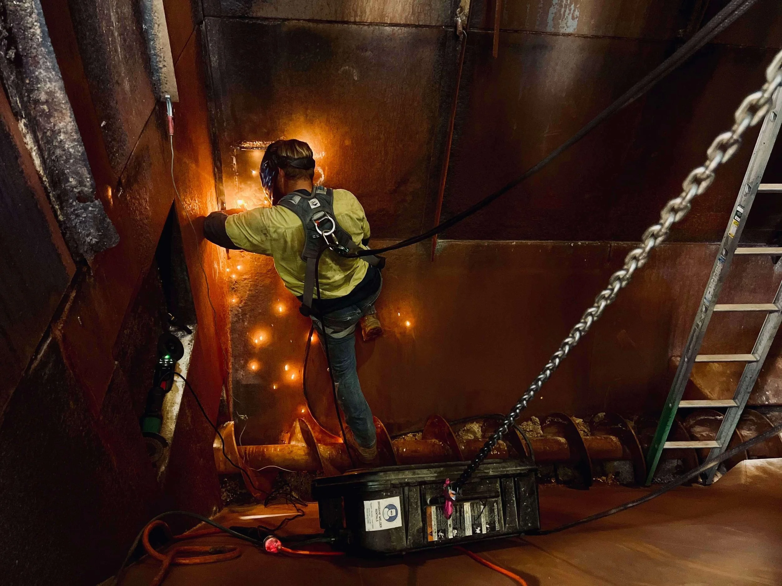 Worker welding inside an industrial tank or vessel with welding equipment and safety gear.