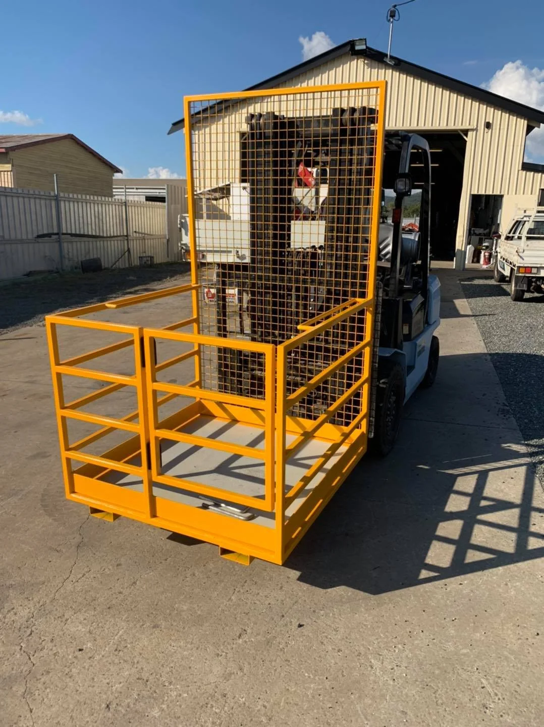 A small forklift with a yellow safety cage attached, parked outside a warehouse with a clear blue sky overhead.