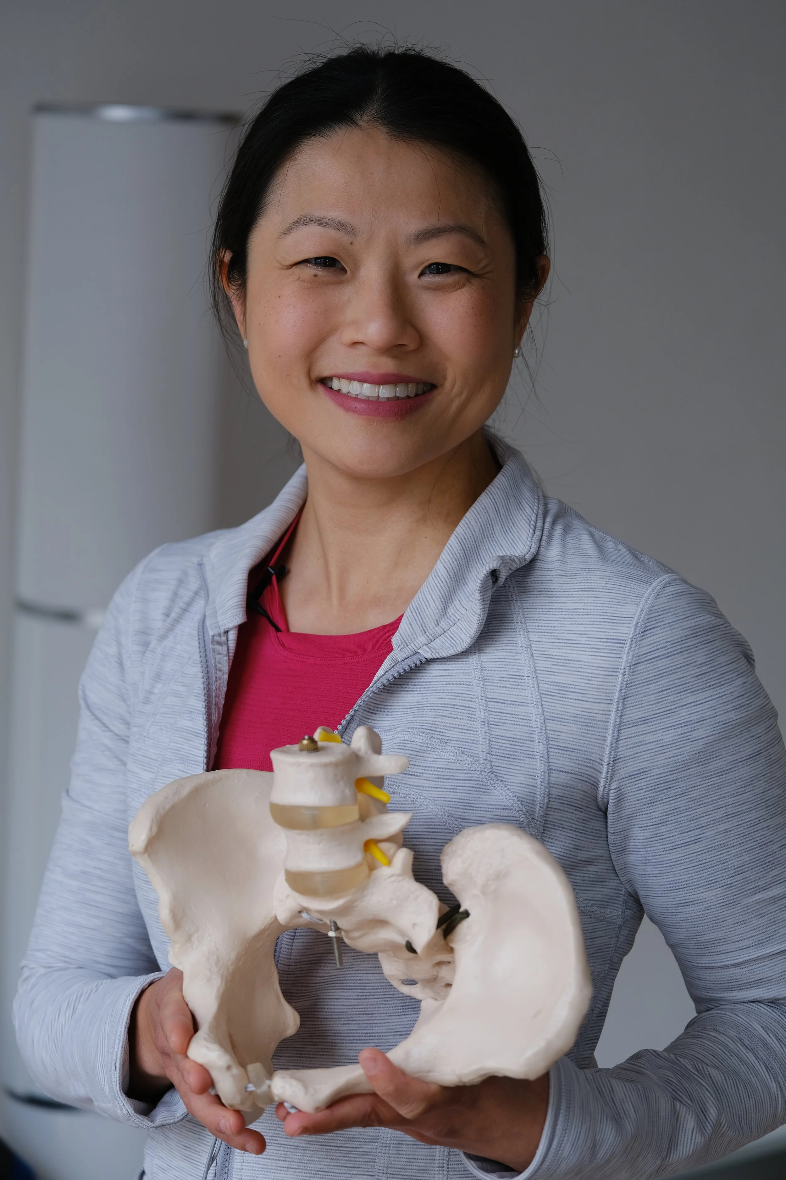 A woman smiling while holding a pelvic bone model with a vertebrae on top.
