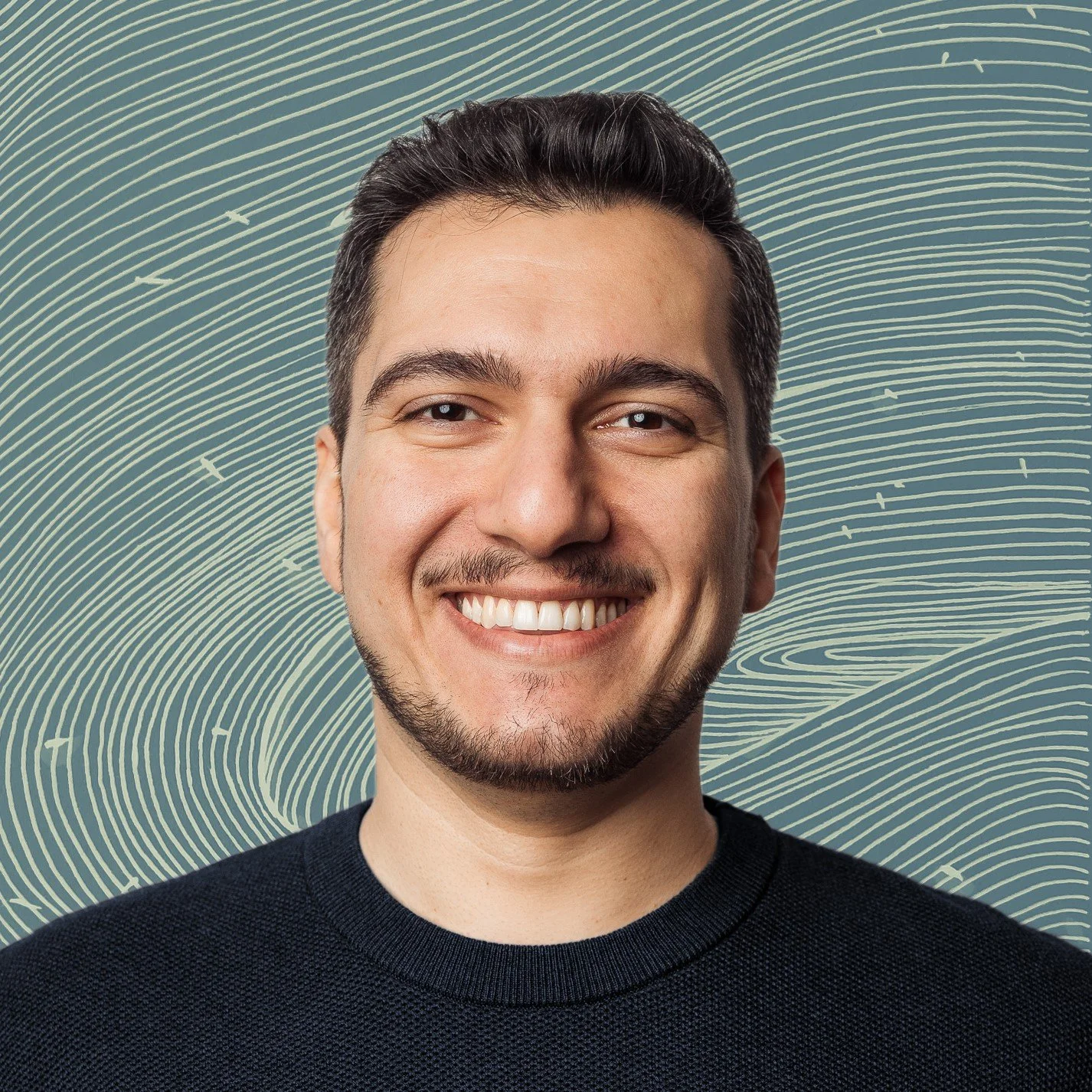 A smiling man with dark hair and facial hair, wearing a dark knitted sweater, against a background with abstract swirling lines.
