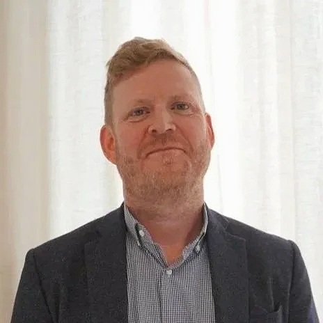 A smiling man wearing a shirt and blazer.