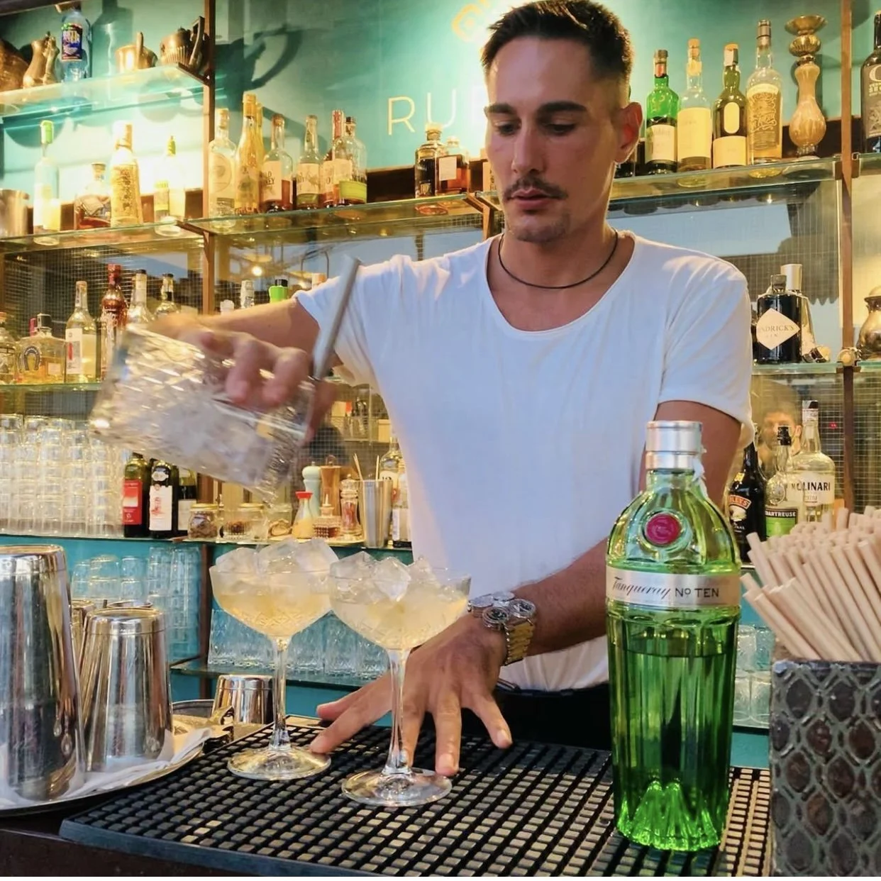 Bartender preparando cócteles en un bar con muchas botellas de alcohol en el fondo.