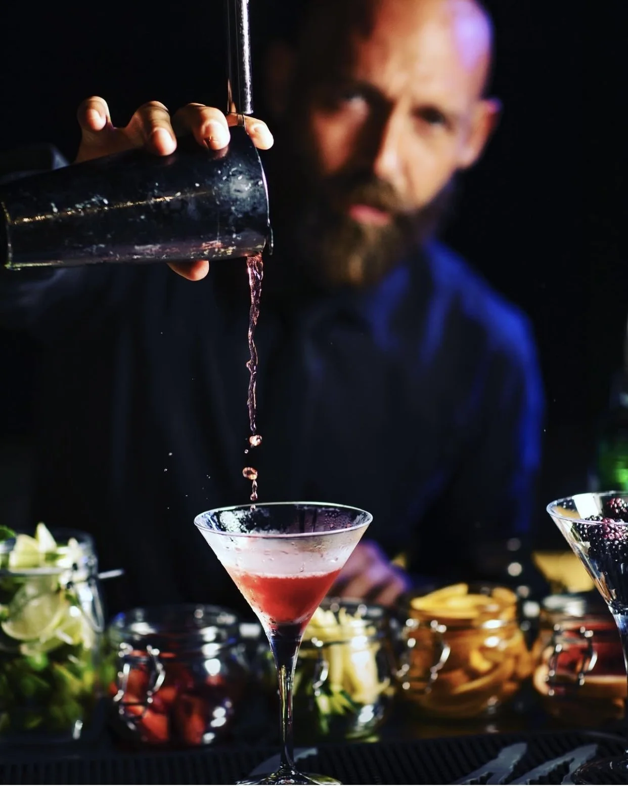 Un bartender vertiendo una bebida color rosa en una copa de cóctel en un bar
