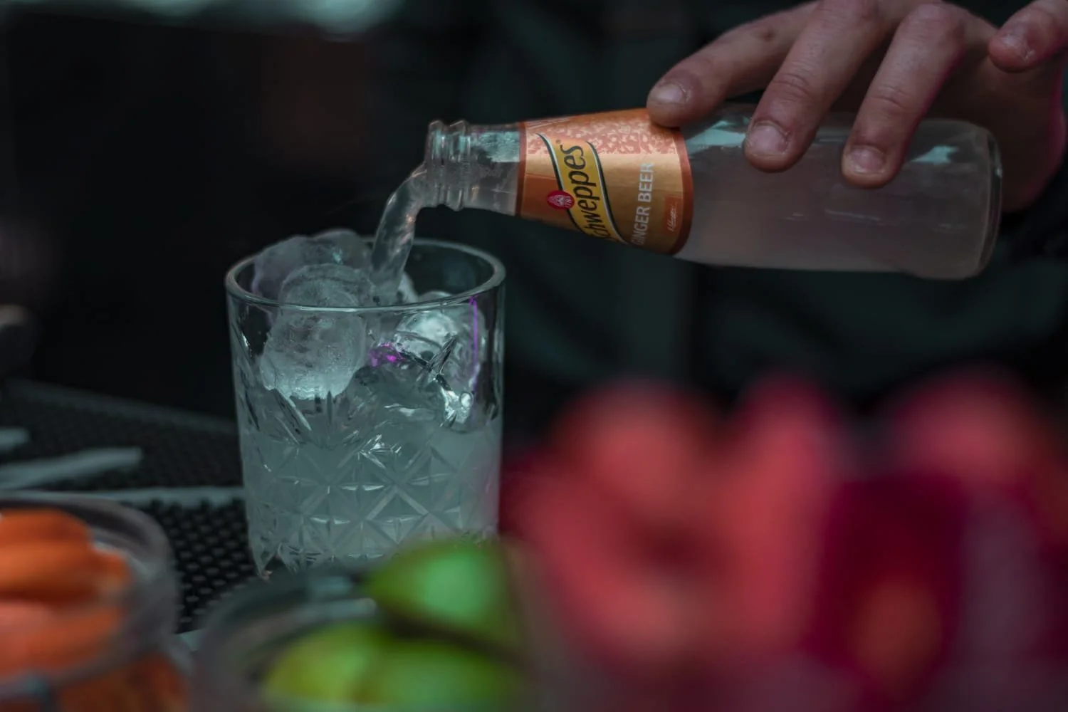 Una mano vierte cerveza de una botella en un vaso con hielo.