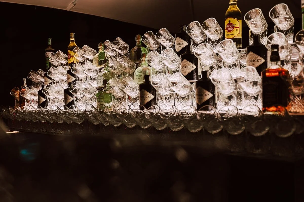 Botellas de licor y vasos en una exposición con iluminación que resalta los cristales.