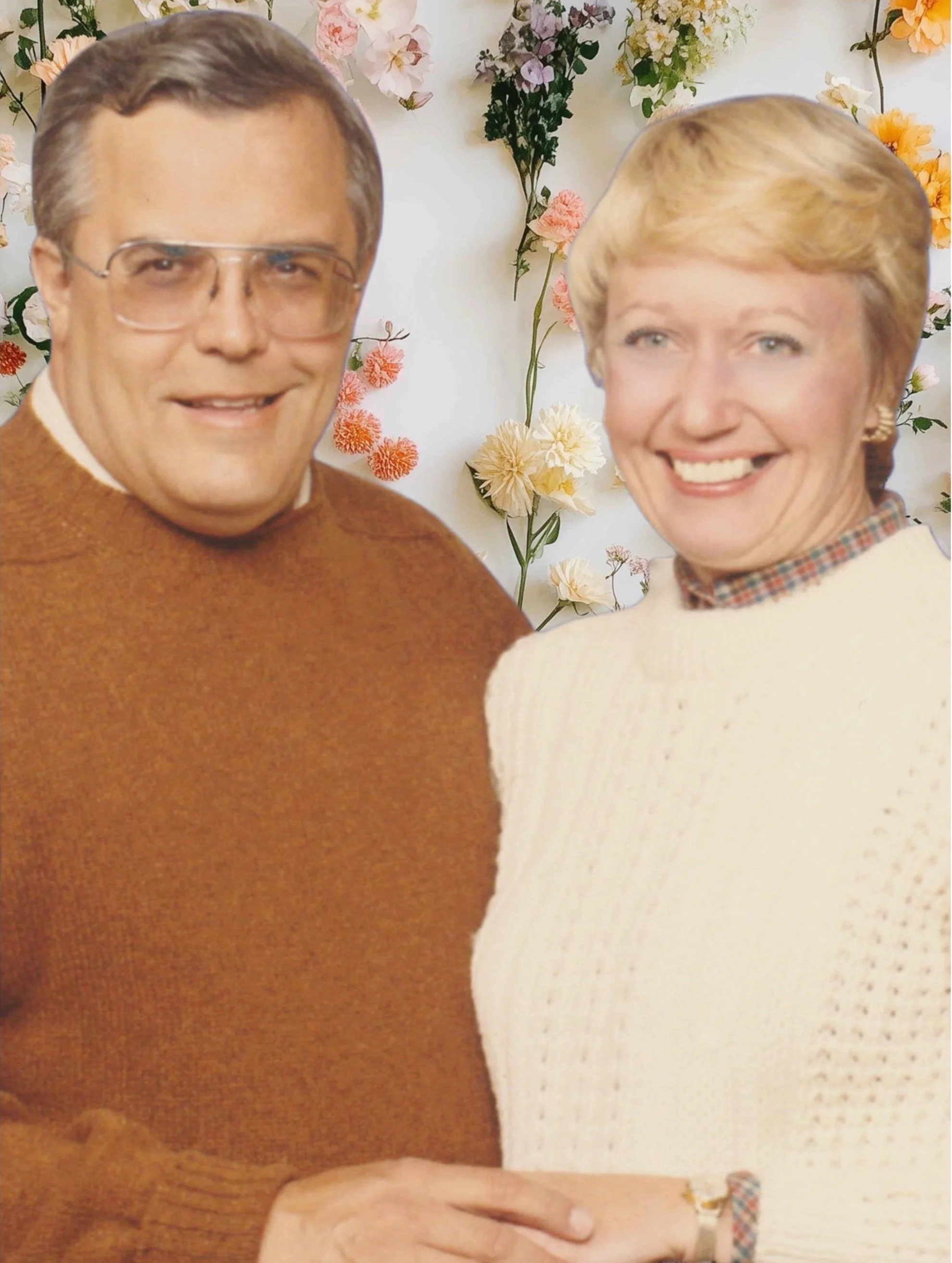 A vintage-style photograph of a smiling middle-aged man and woman standing close together outdoors with a background of pink, white, yellow, and purple flowers in bloom.