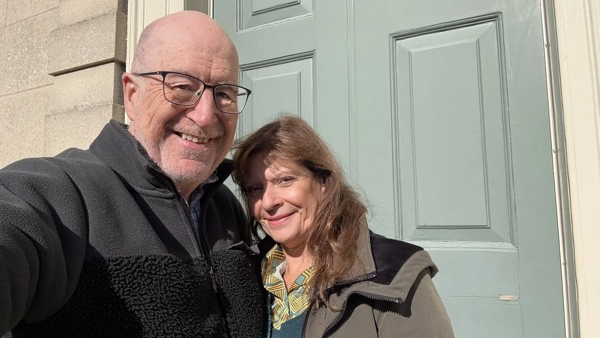Colin Newton and Jacqui Newton, Inclusive Solutions trainers, smiling outside a green front door