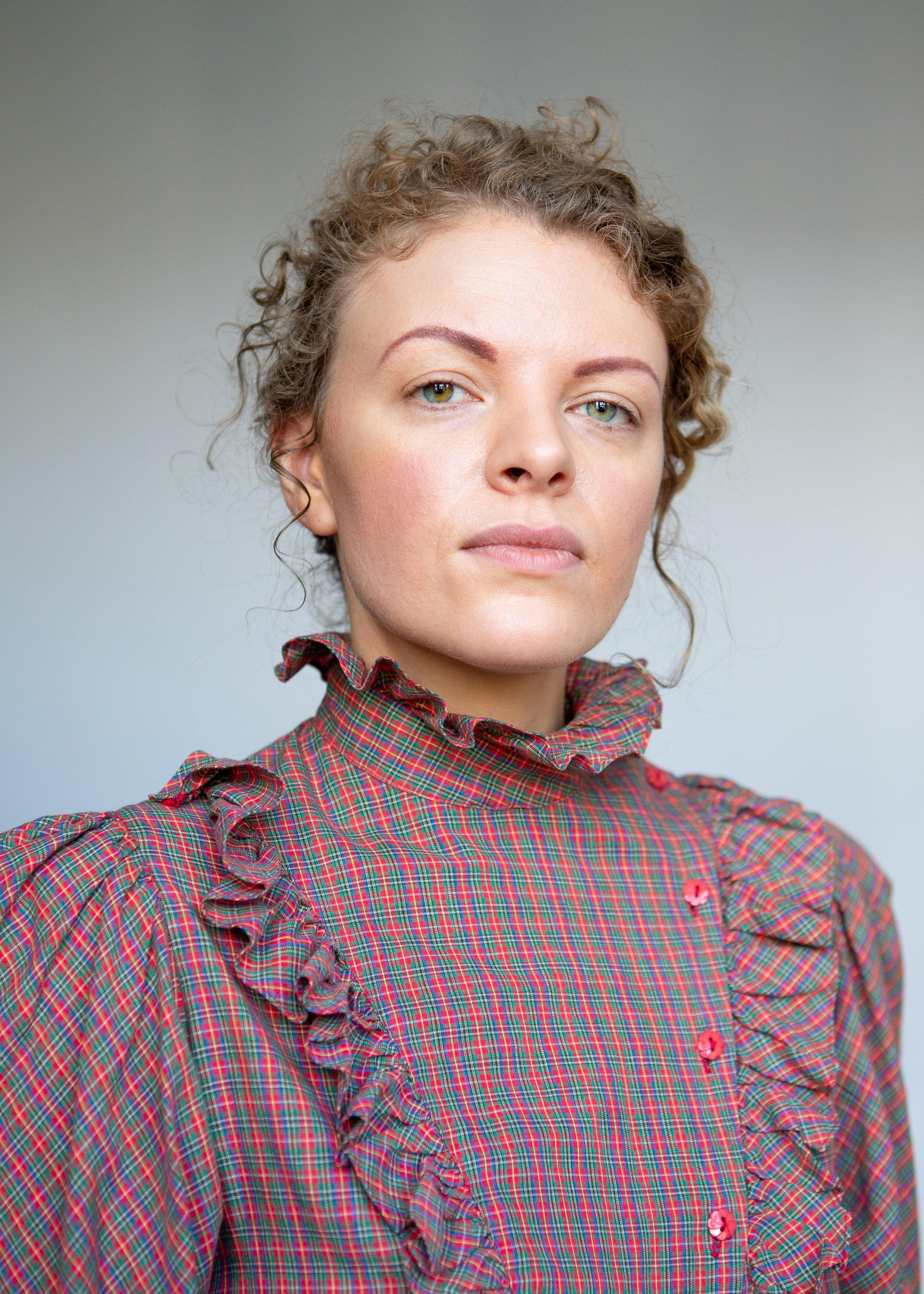 Person wearing a red plaid ruffled blouse looking confidently at the camera, with a neutral background.