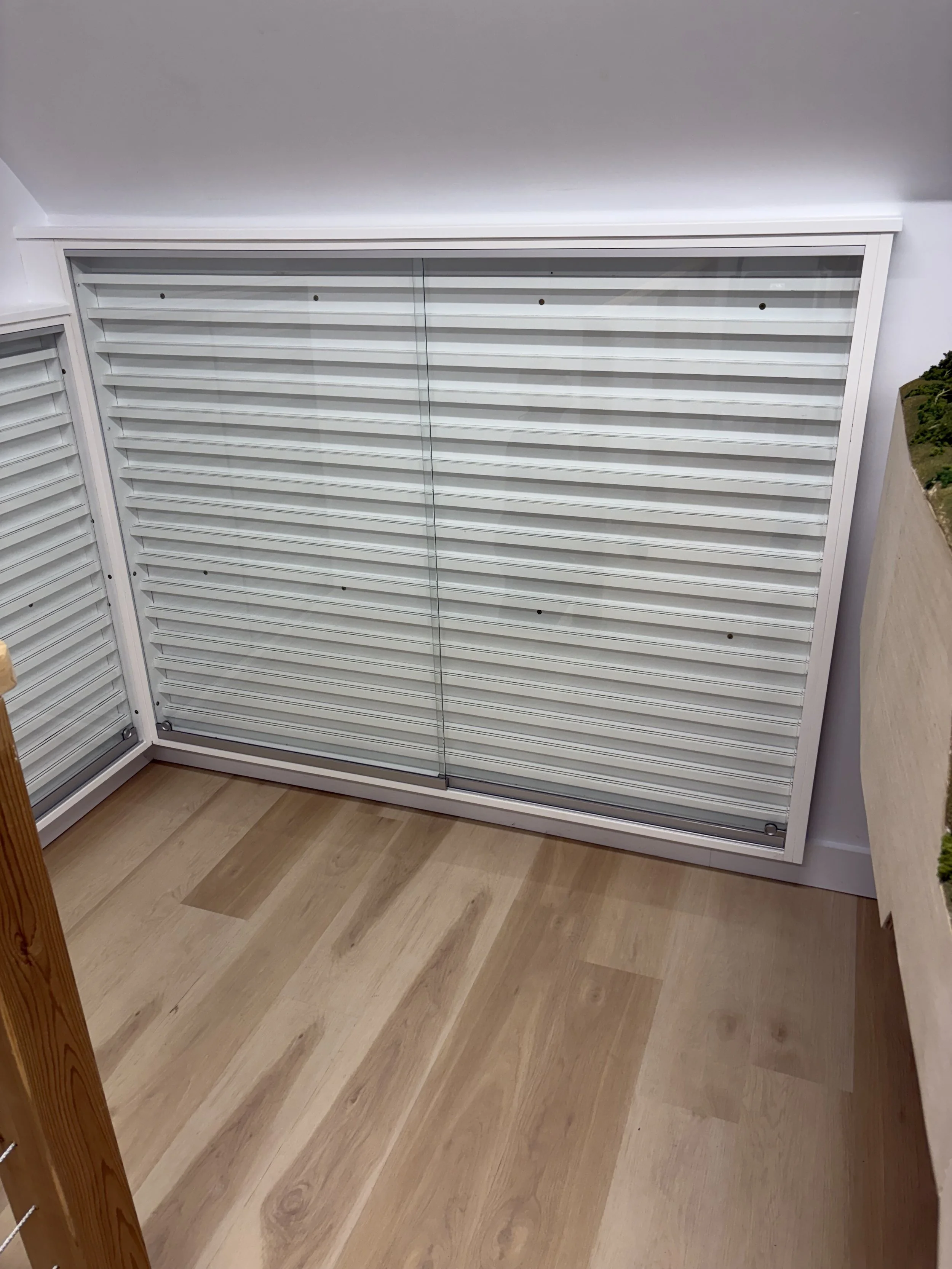 A white storage cabinet with sliding glass doors and horizontal white slats inside, positioned against a wall on hardwood flooring.