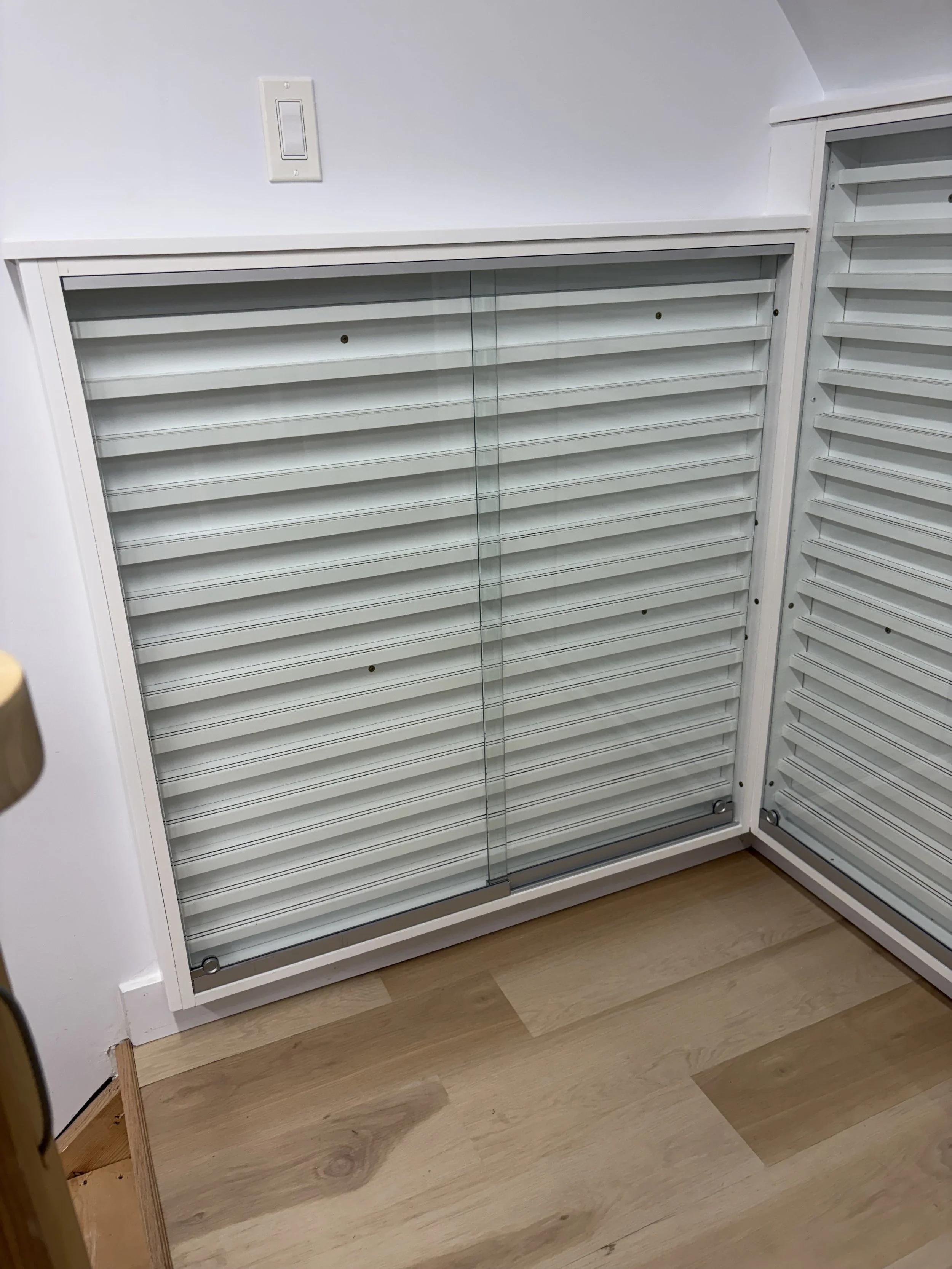 White cabinet with multiple slatted drawers and glass sliding doors, situated on a wooden floor.