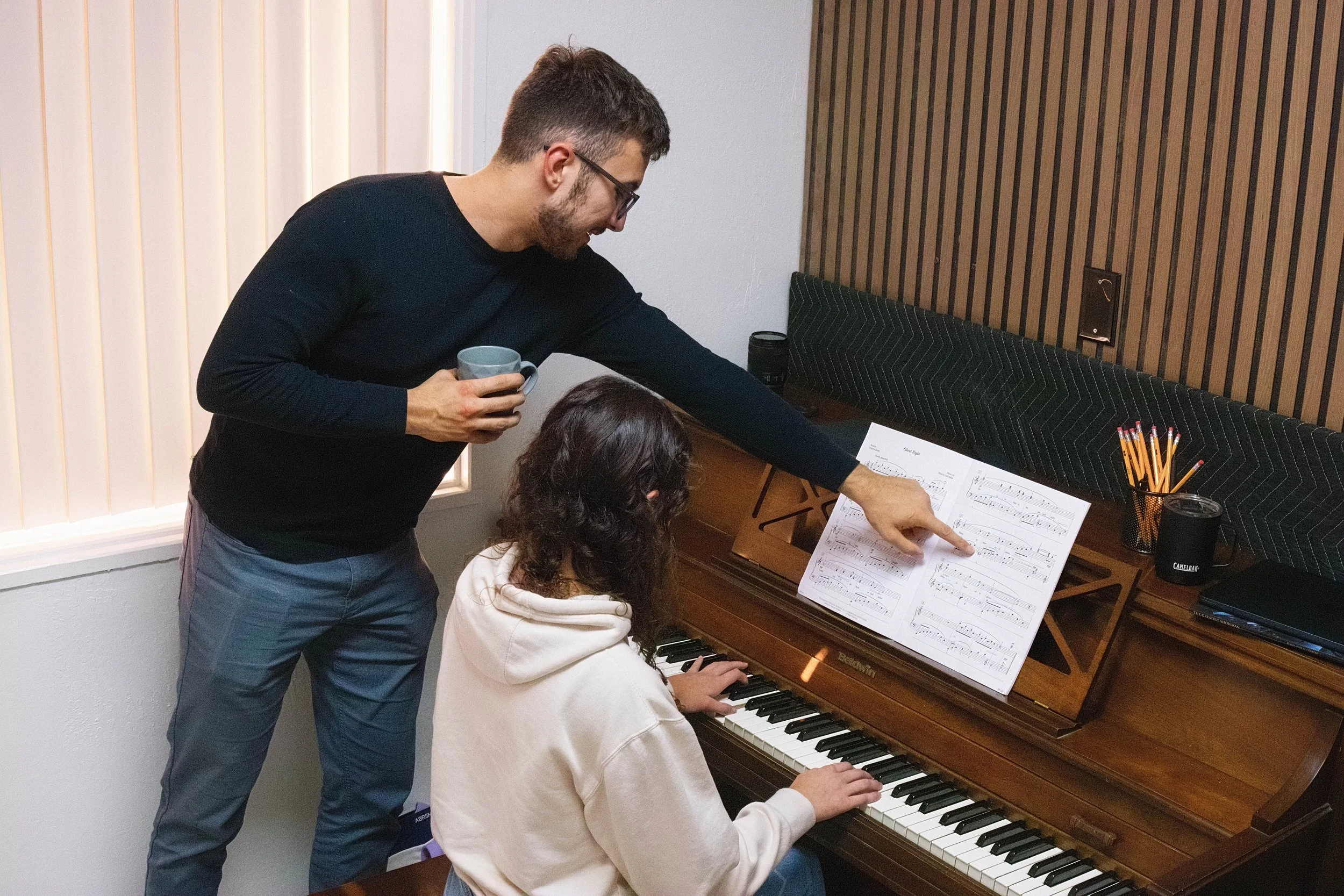 A young girl and a woman, possibly a teacher, are smiling and looking at each other in a library surrounded by bookshelves.