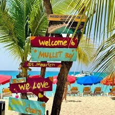 Panneaux colorés sur une plage, avec des palmiers, des chaises longues et des parasols bleus et rouges en arrière-plan à Mullet Bay, Saint-Martin.
