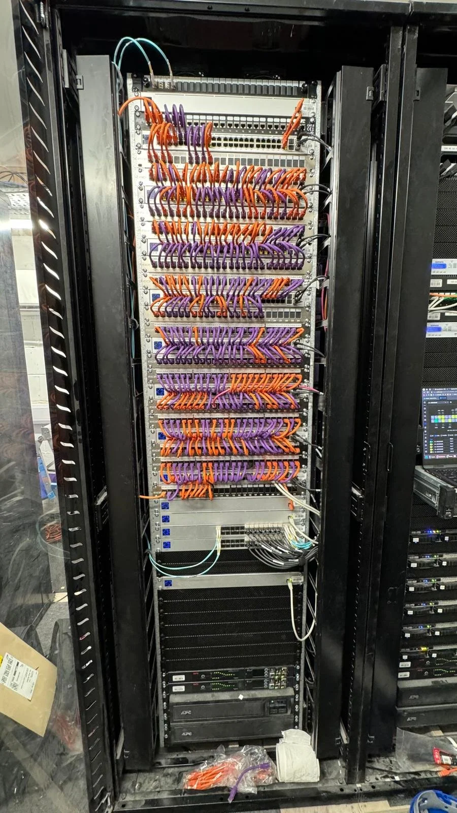 A server rack with various network cables, including purple and orange Ethernet cables, connected to networking equipment.