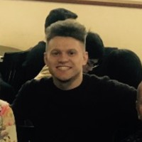 A young man with short hair smiling, seated indoors at a social event