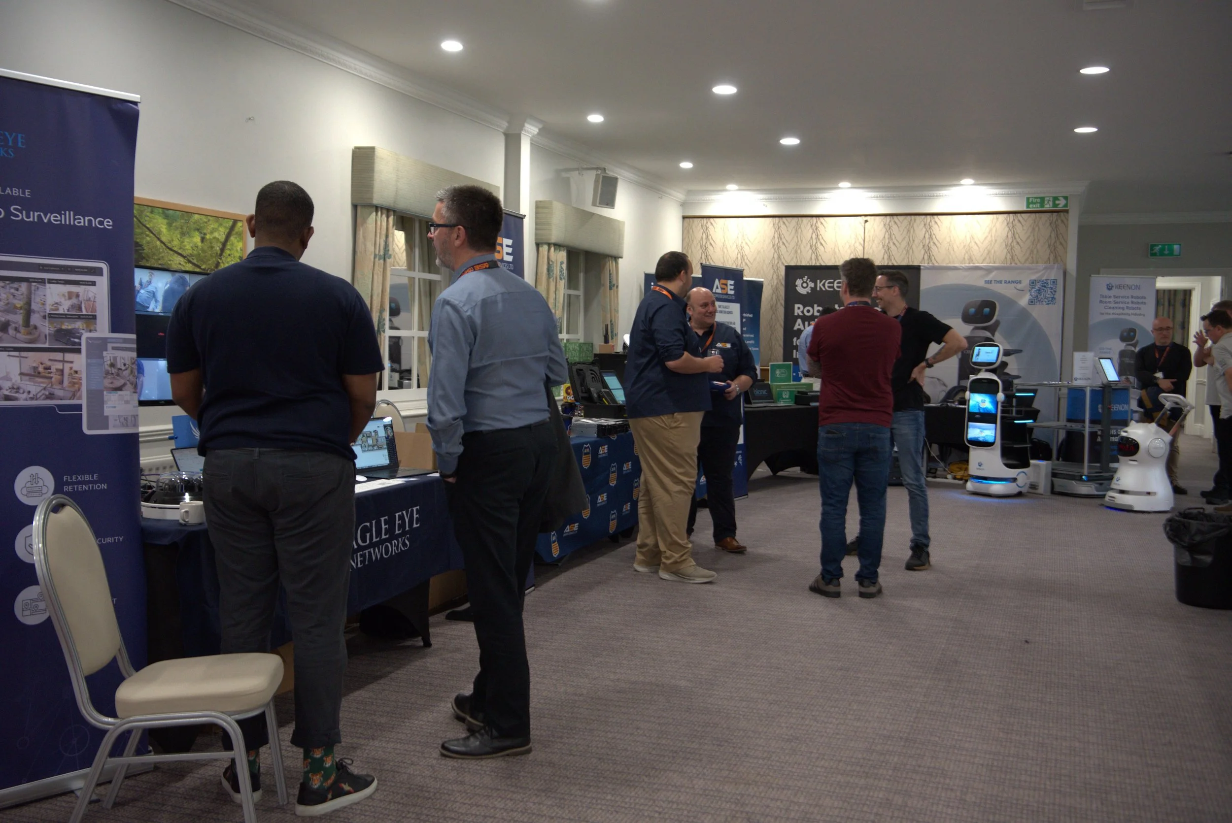 Attendees at a technology exhibition or conference booth with robotic and surveillance equipment, engaging in conversations.