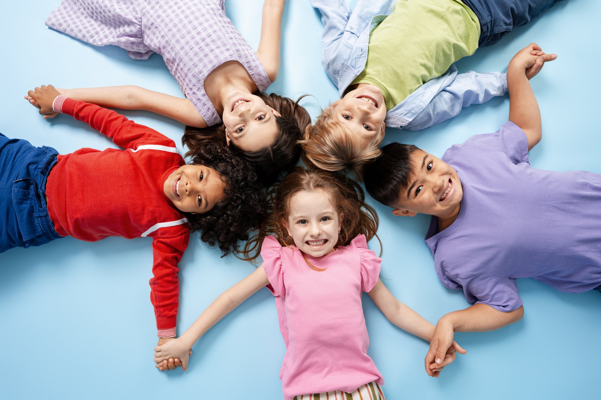 Group of children lying on a blue surface, holding hands, and smiling at the camera.