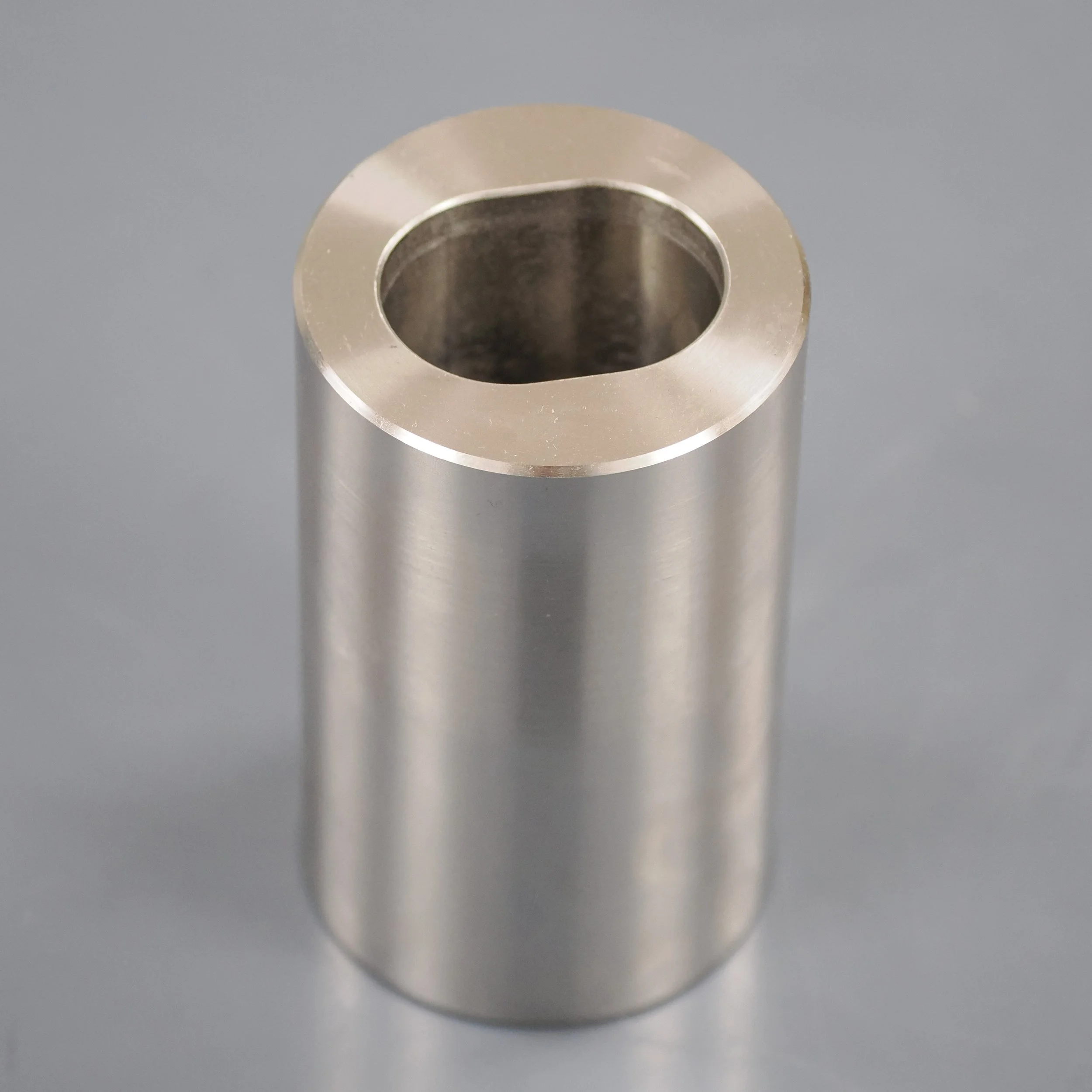 Close-up of a metallic hollow cylindrical object with smooth surface, placed on a gray background.