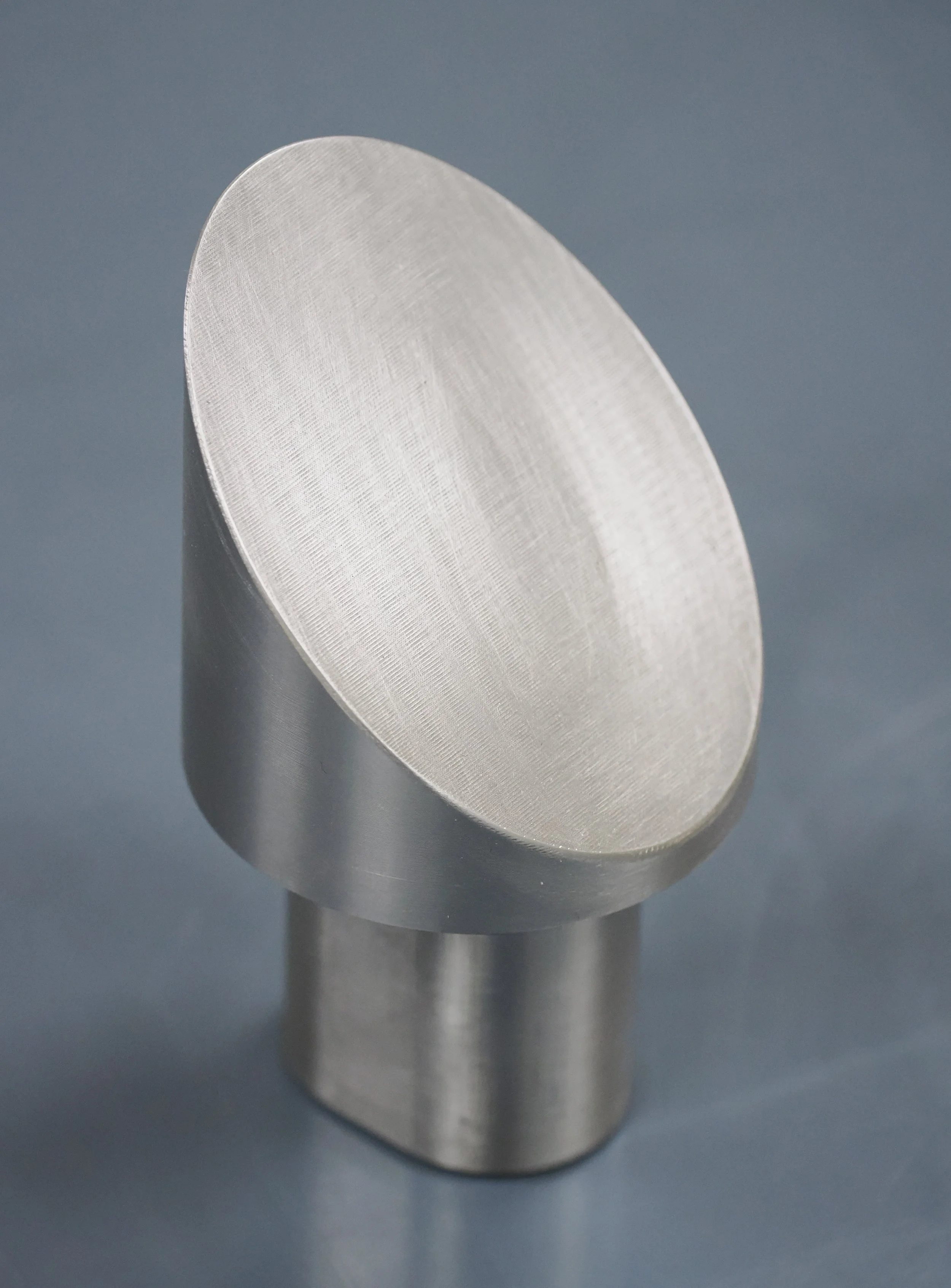 Close-up view of a metallic, cylindrical object with a rounded top, positioned on a gray surface.