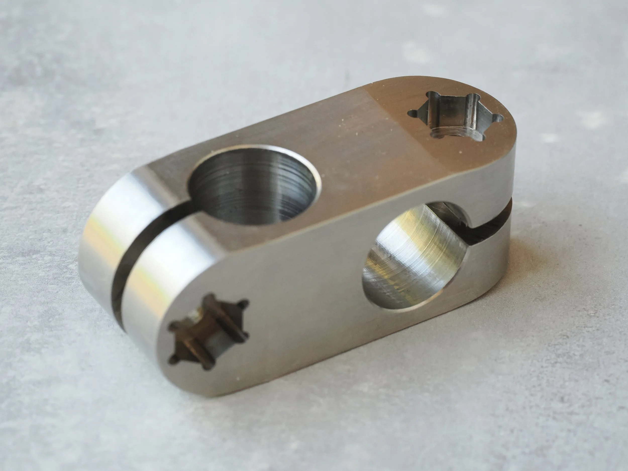 Close-up view of a metallic mechanical component with threaded holes and a star-shaped tool slot on top, placed on a flat surface.